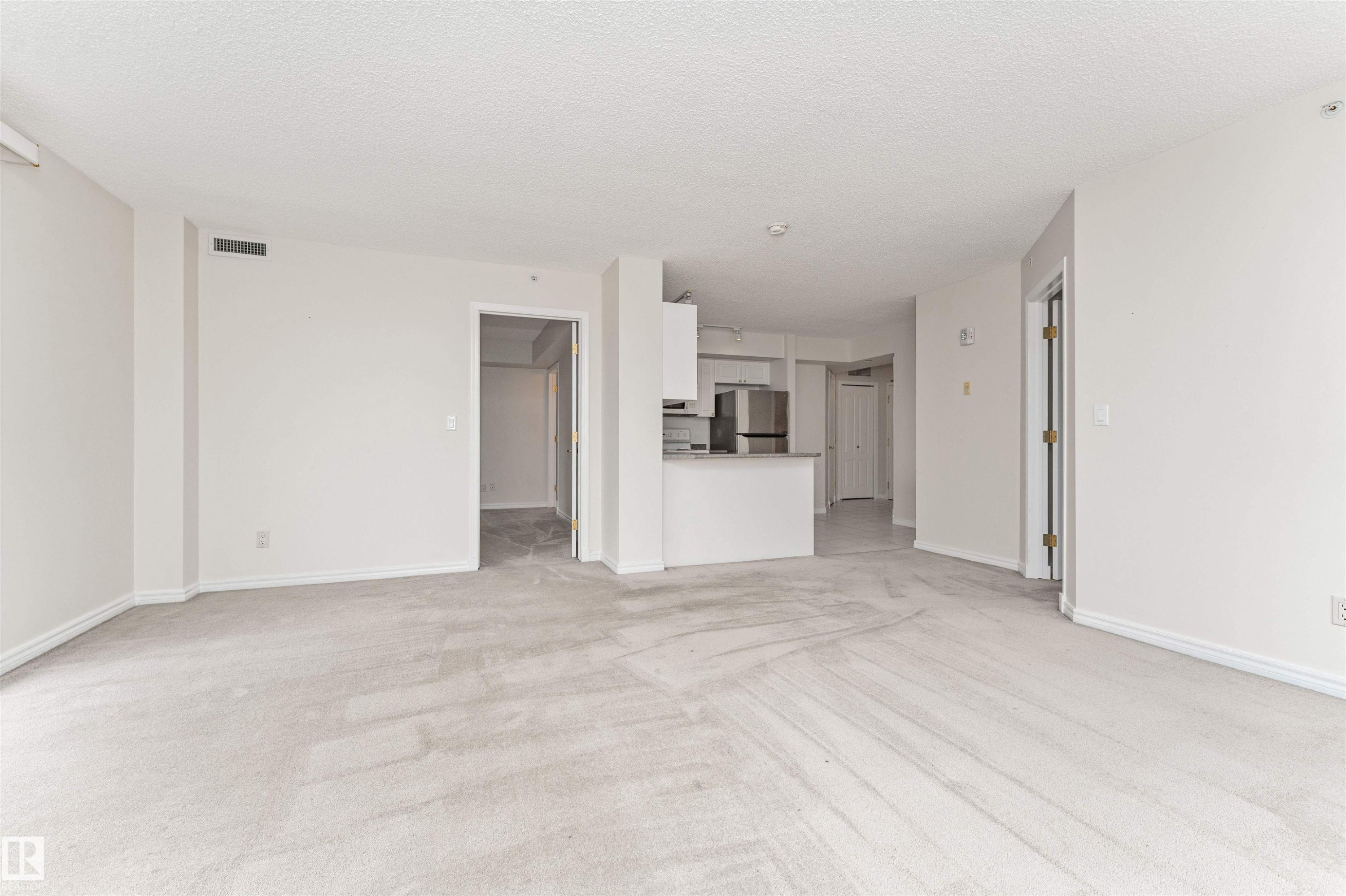 Expansive open-concept living area with light-colored carpeting, recessed lighting, and a white kitchen with stainless steel appliances - #1101 10909 103 Av Nw, Edmonton, AB - Indoor