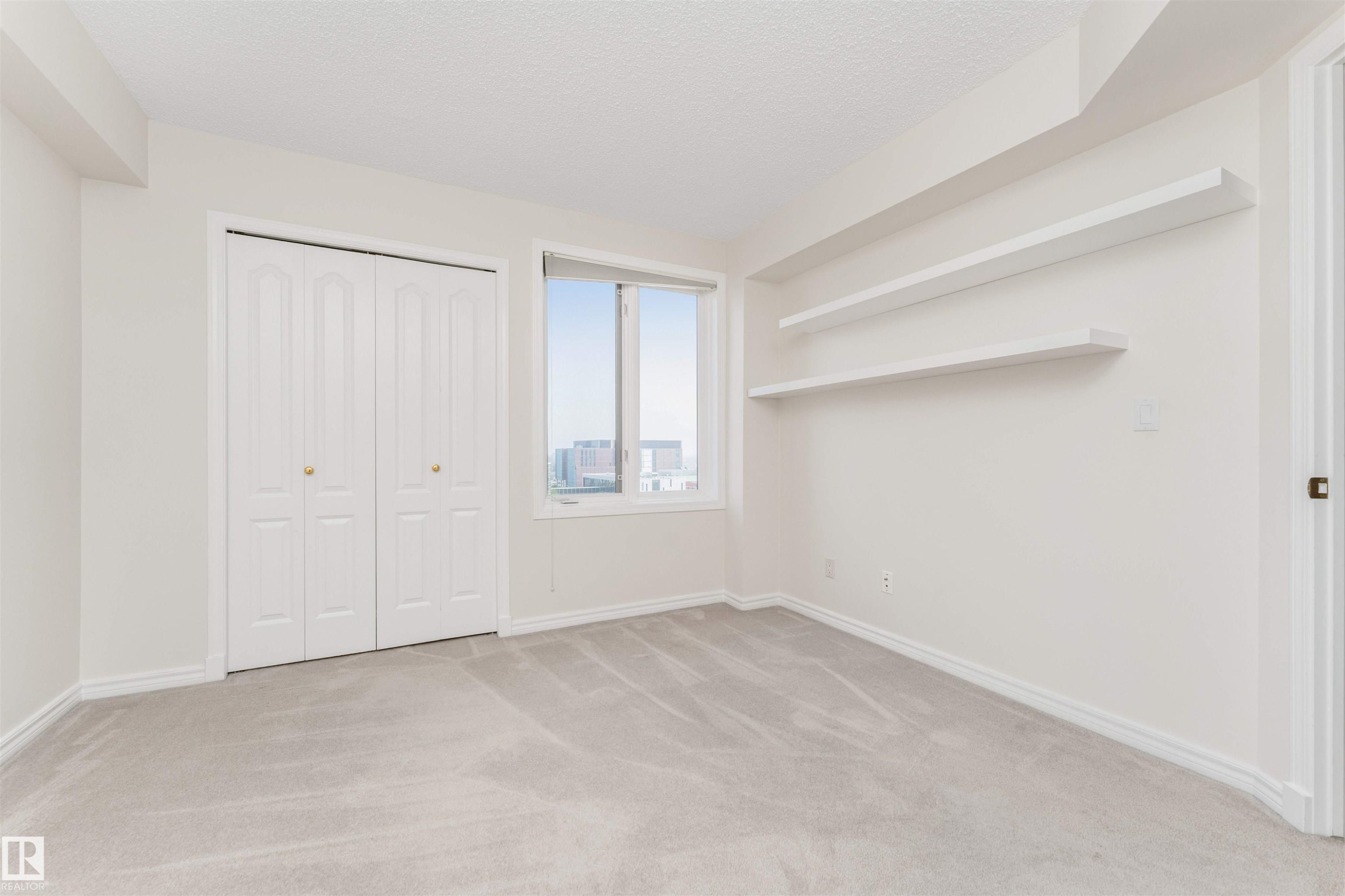 Light-toned wall-to-wall carpeting, white walls, built-in shelving, white bi-fold closet doors, and an exterior window - #1101 10909 103 Av Nw, Edmonton, AB - Indoor Photo Showing Other Room