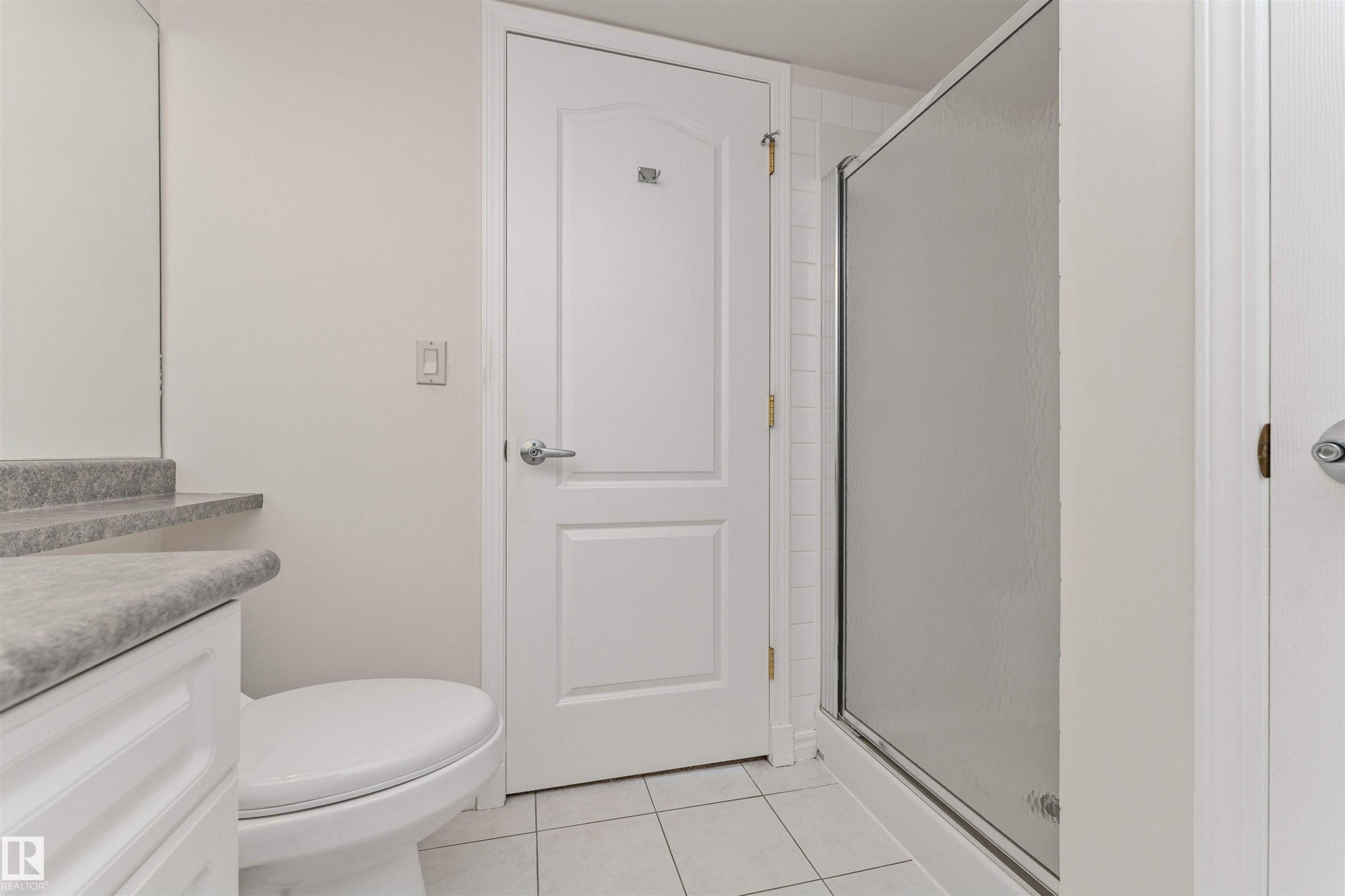 White vanity with a stone-finish countertop, white toilet, and enclosed shower with a translucent glass door - #1101 10909 103 Av Nw, Edmonton, AB - Indoor Photo Showing Bathroom