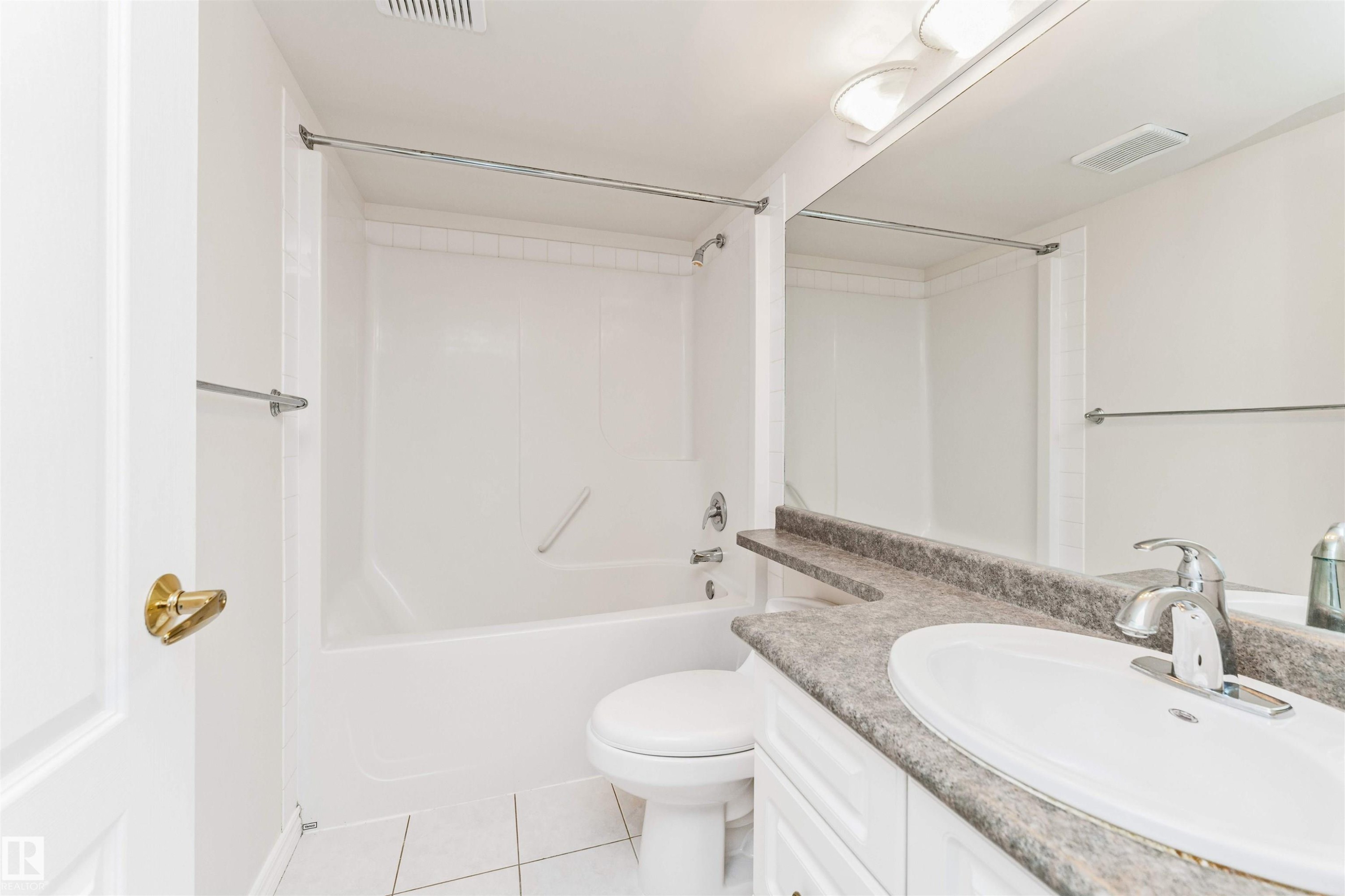 White bathroom featuring a bathtub with shower, white toilet, vanity with integrated sink, and a large mirror - #1101 10909 103 Av Nw, Edmonton, AB - Indoor Photo Showing Bathroom