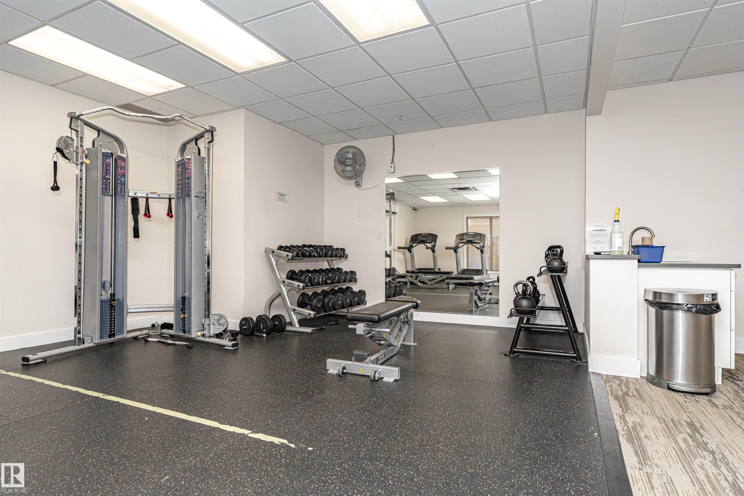 Fitness area with rubberized flooring, mirrored wall, recessed lighting, and built-in counter with sink - #1101 10909 103 Av Nw, Edmonton, AB - Indoor Photo Showing Gym Room