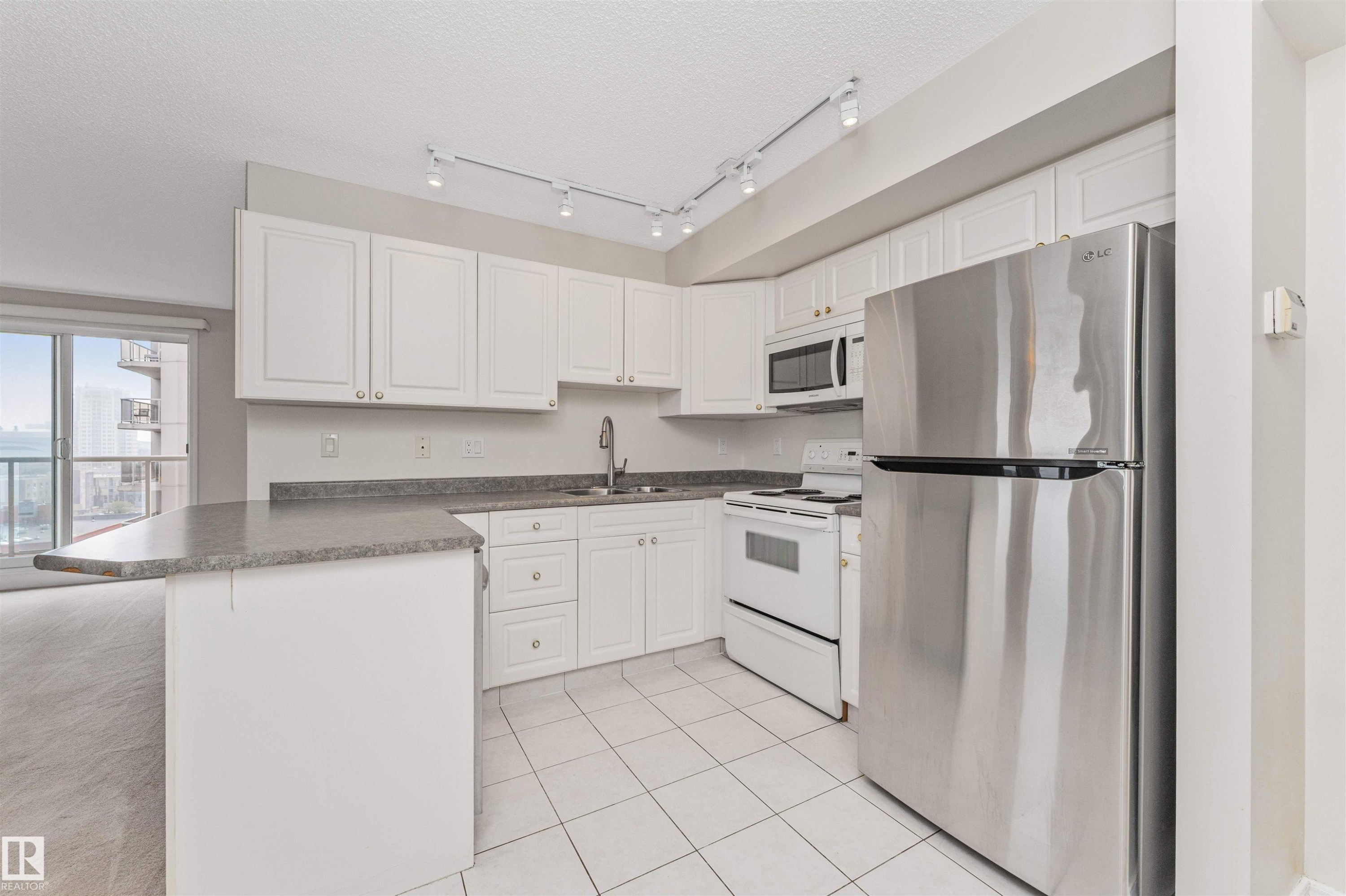 Kitchen featuring white cabinetry, gray countertops, stainless steel refrigerator, white range, and white tiled flooring - #1101 10909 103 Av Nw, Edmonton, AB - Indoor Photo Showing Kitchen With Double Sink