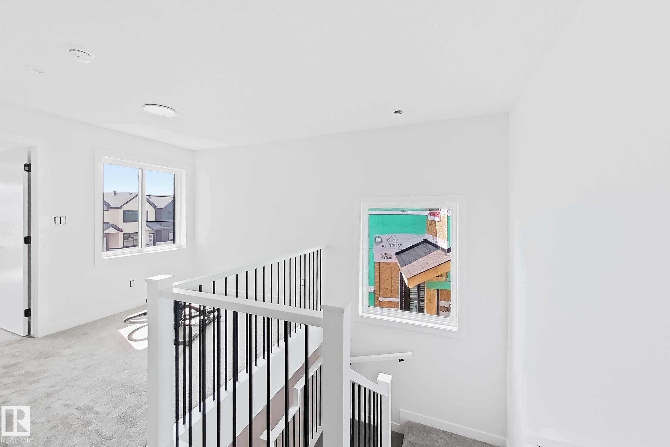 White painted walls with white trim, a staircase featuring white newel posts and handrails with black metal balusters, and light gray carpeted flooring - 13118 186 Avenue Nw, Edmonton, AB - Indoor Photo Showing Other Room
