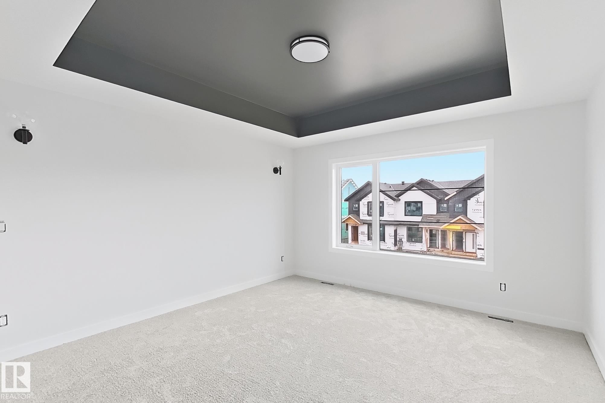 Tray ceiling with contrasting finish, contemporary flush mount lighting, white-painted walls, light-colored carpeting, and a large window - 13118 186 Avenue Nw, Edmonton, AB - Indoor Photo Showing Other Room