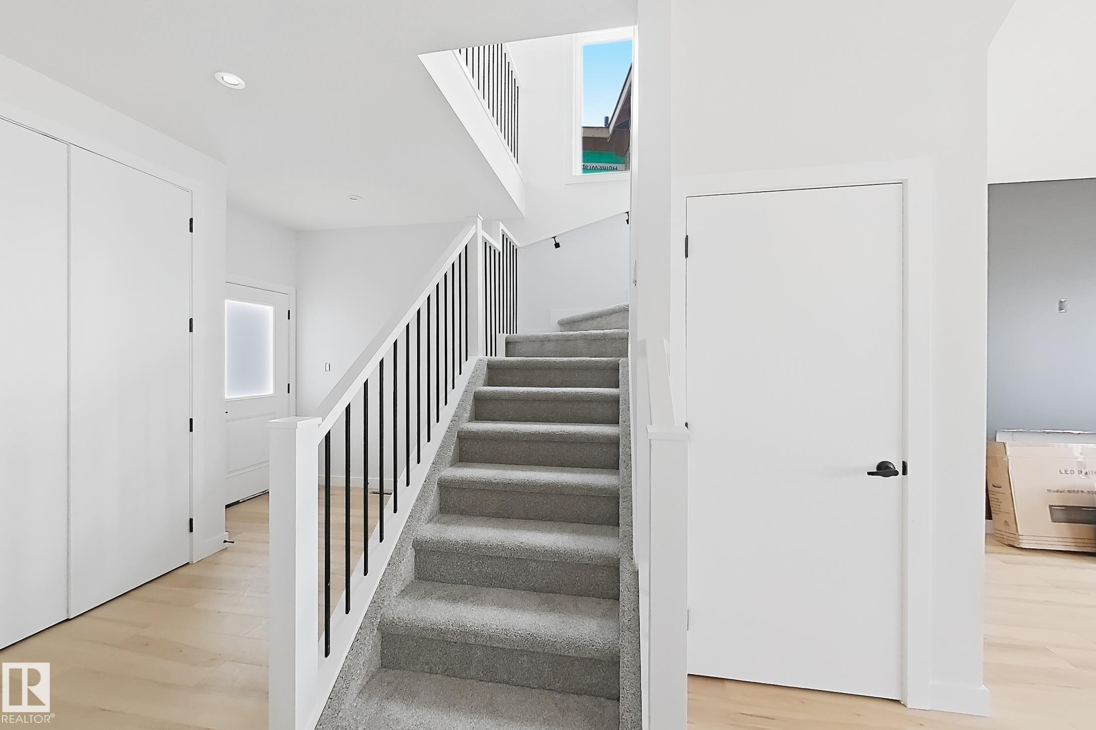 Wood-finish flooring, recessed lighting, white walls, and a staircase with carpeted treads and black metal balusters - 13118 186 Avenue Nw, Edmonton, AB - Indoor Photo Showing Other Room
