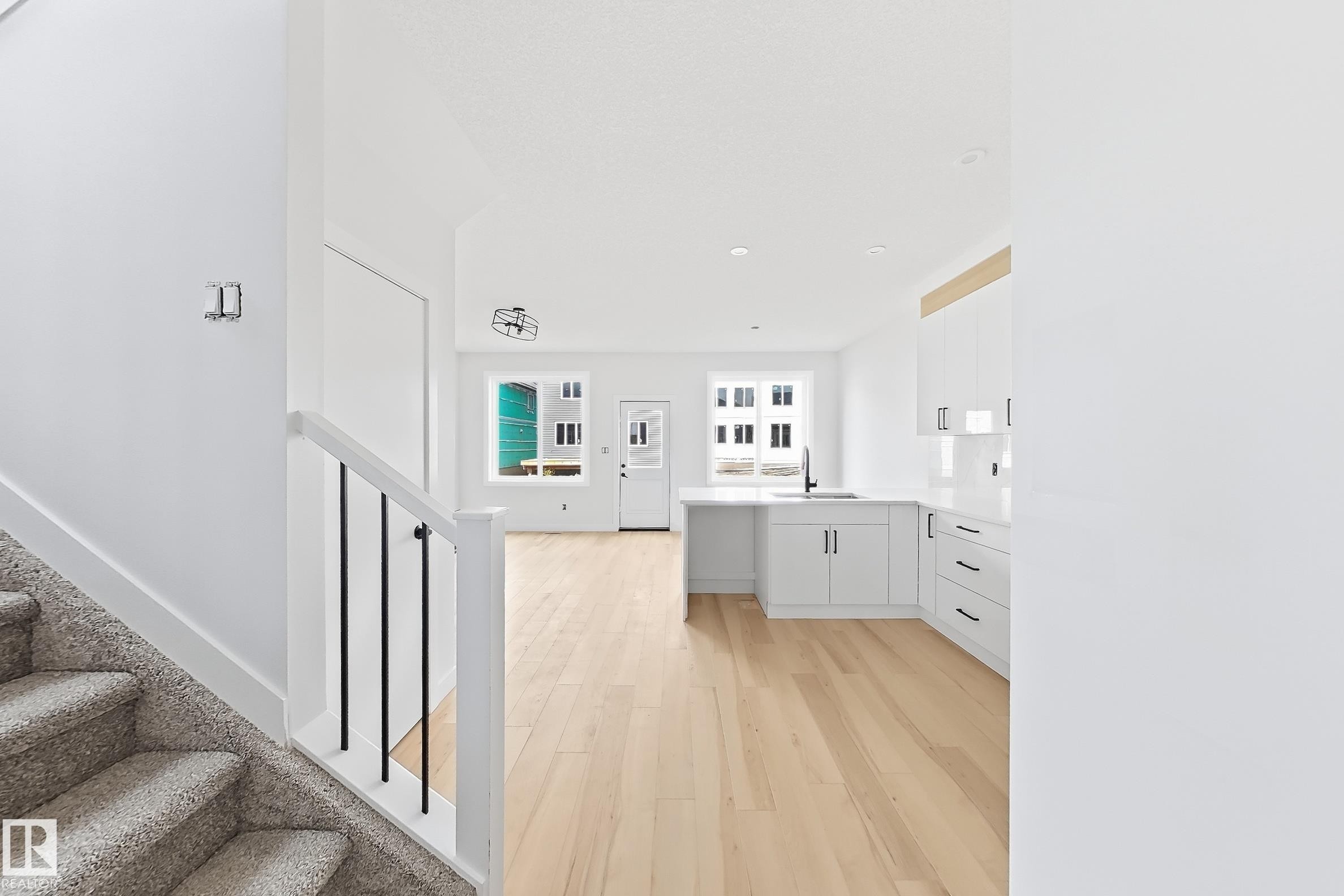 Open-concept design featuring wood-finish flooring, white cabinetry, and a kitchen island with a black faucet - 13118 186 Avenue Nw, Edmonton, AB - Indoor