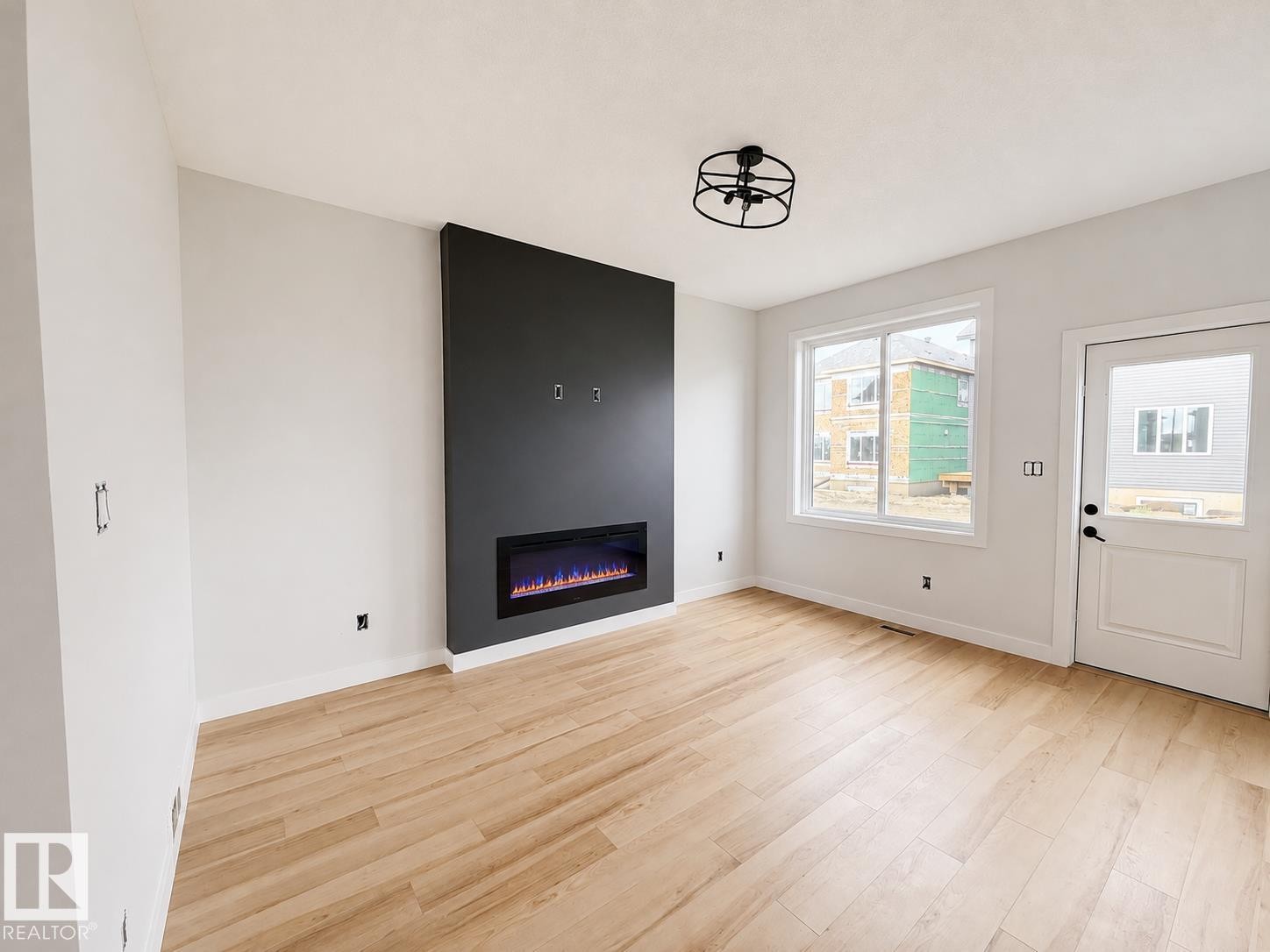 Contemporary electric fireplace with a dark accent wall, light wood-finish flooring, and a modern semi-flush mount ceiling fixture - 13118 186 Avenue Nw, Edmonton, AB - Indoor With Fireplace