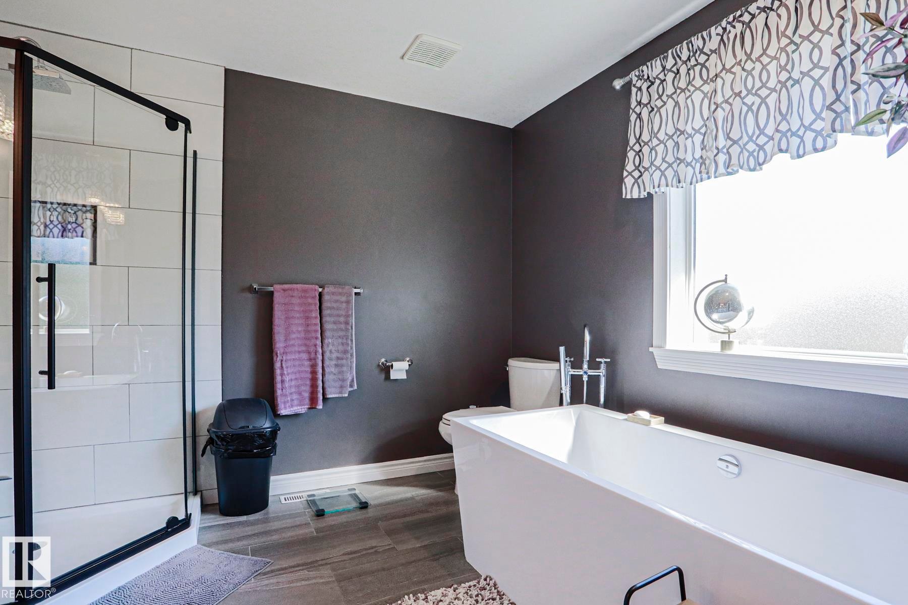 Freestanding soaking tub, glass-enclosed shower with white tiled surround, and a large window with privacy glass - 12 Douziech Close, St. Albert, AB - Indoor Photo Showing Bathroom