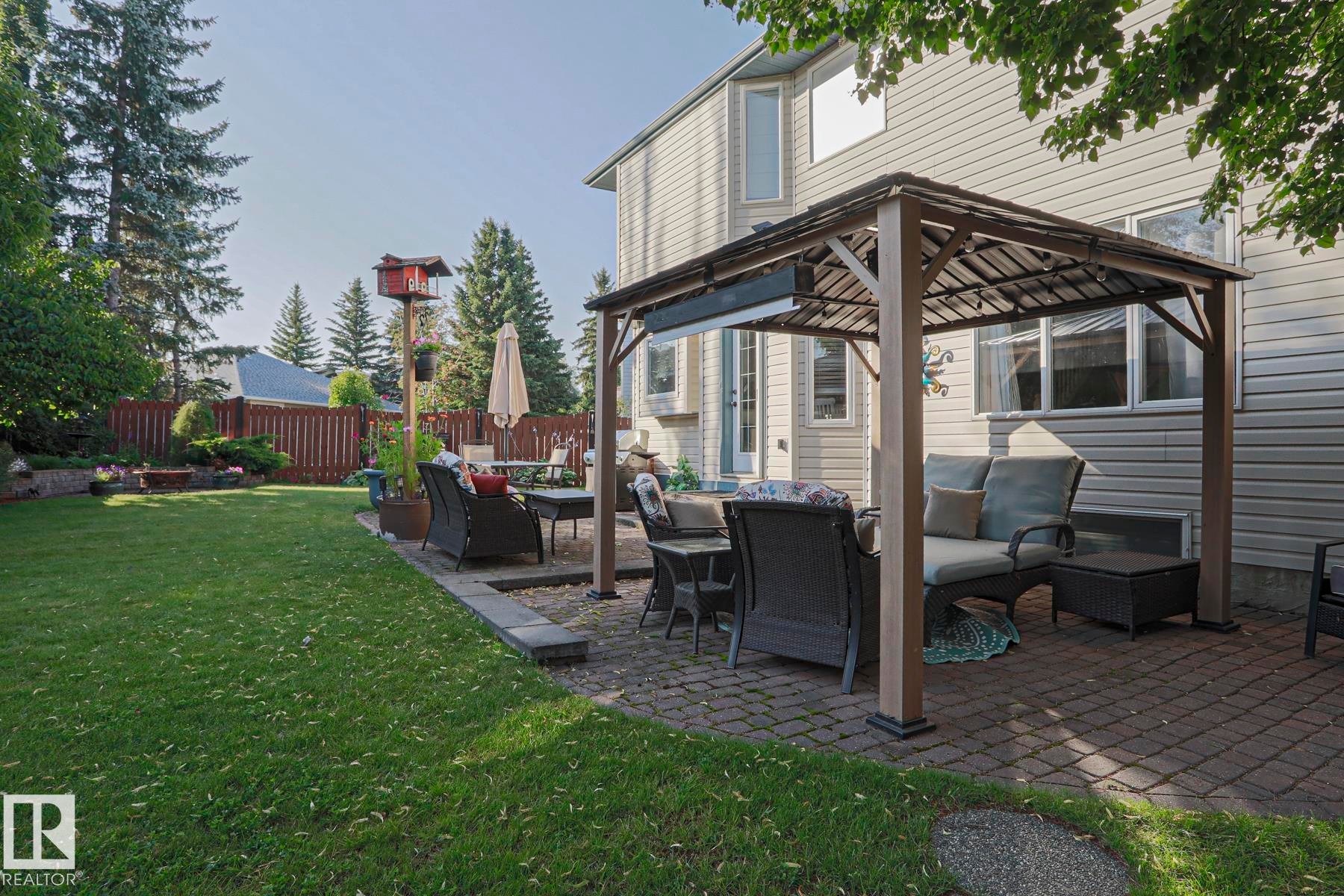Expansive backyard featuring a large lawn, a paved patio with a gazebo, and privacy fencing - 12 Douziech Close, St. Albert, AB - Outdoor With Deck Patio Veranda With Exterior