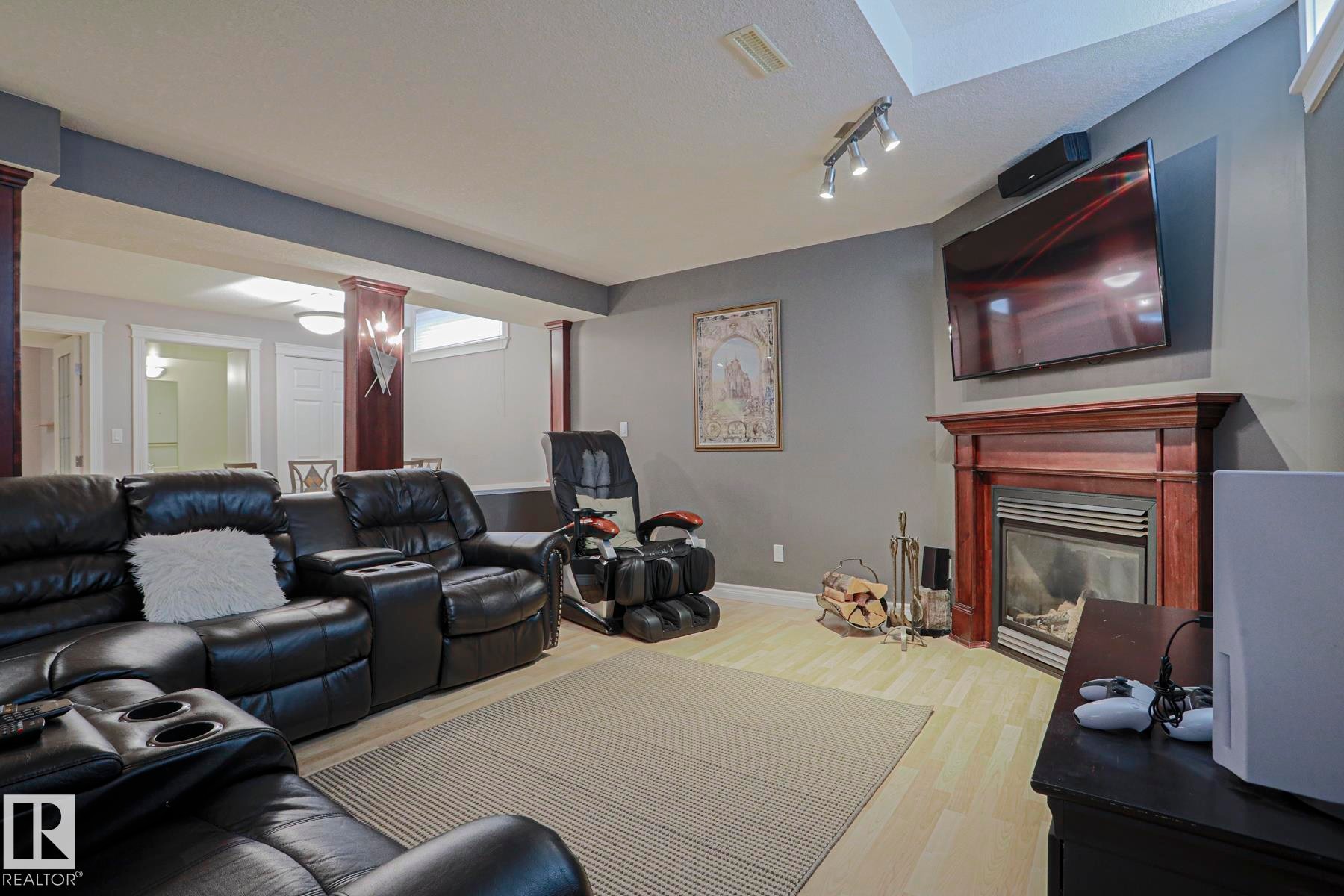 Recessed ceiling with track lighting, wood-finish flooring, built-in fireplace with wood surround, and supporting columns with wood detailing - 12 Douziech Close, St. Albert, AB - Indoor Photo Showing Living Room With Fireplace