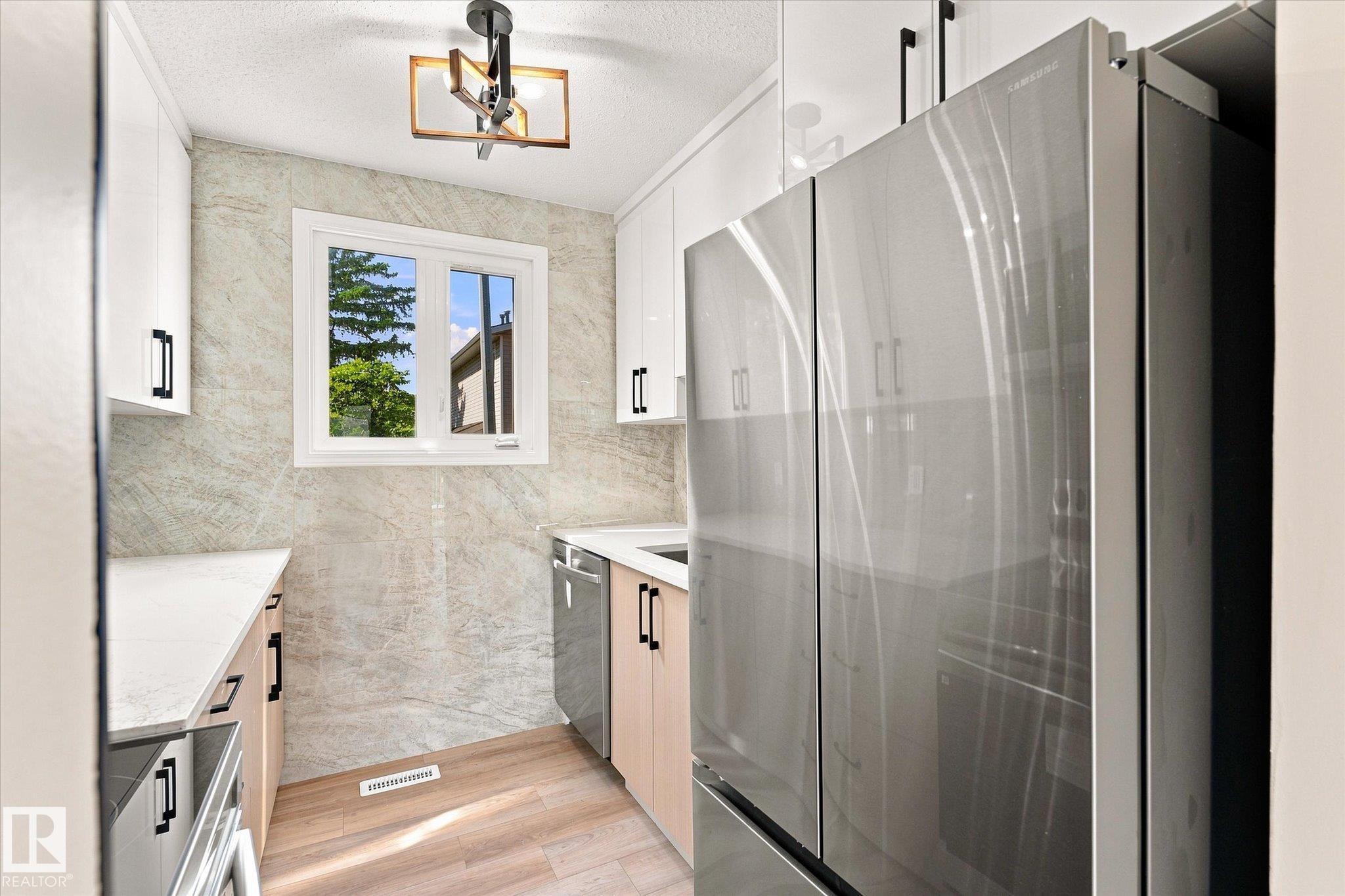 Stainless steel French door refrigerator, wood-finish flooring, white cabinetry, integrated dishwasher, and a window with exterior views - 18307 66 Avenue Nw, Edmonton, AB - Indoor