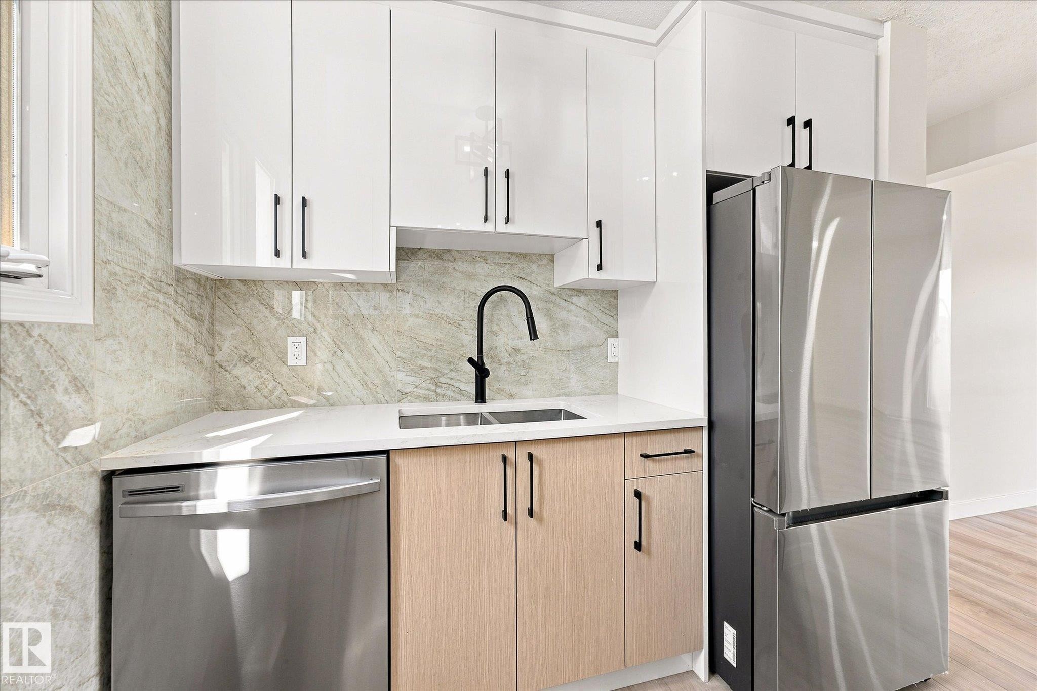 Sleek kitchen featuring white upper cabinetry, light wood-finish lower cabinetry, a stainless steel refrigerator, and a stainless steel dishwasher - 18307 66 Avenue Nw, Edmonton, AB - Indoor Photo Showing Kitchen With Double Sink With Upgraded Kitchen