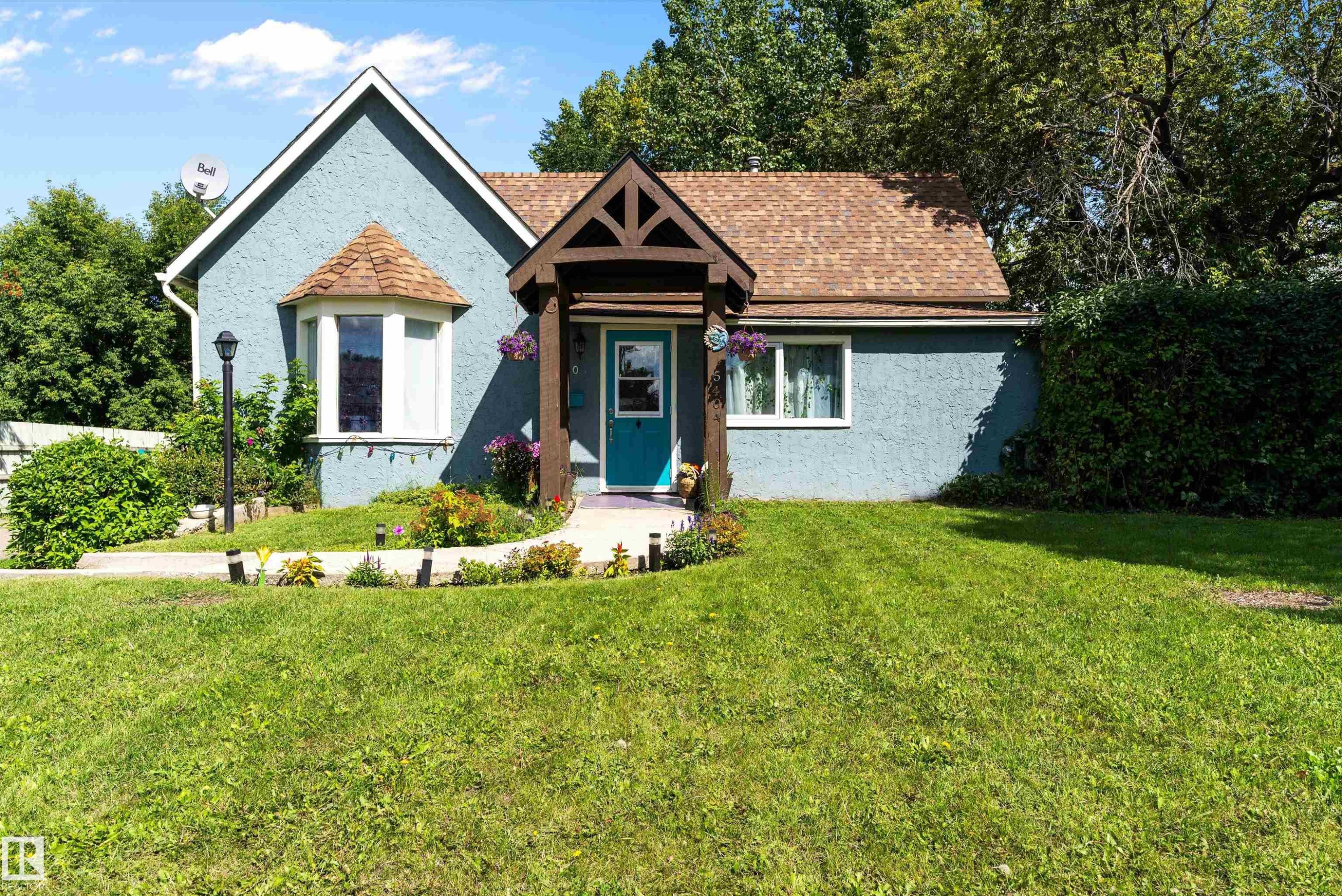 Freshly painted stucco exterior with a peaked roofline, bay window, covered entry, manicured lawn and gorgous flowers. - 5404 45 Avenue, Wetaskiwin, AB - Outdoor