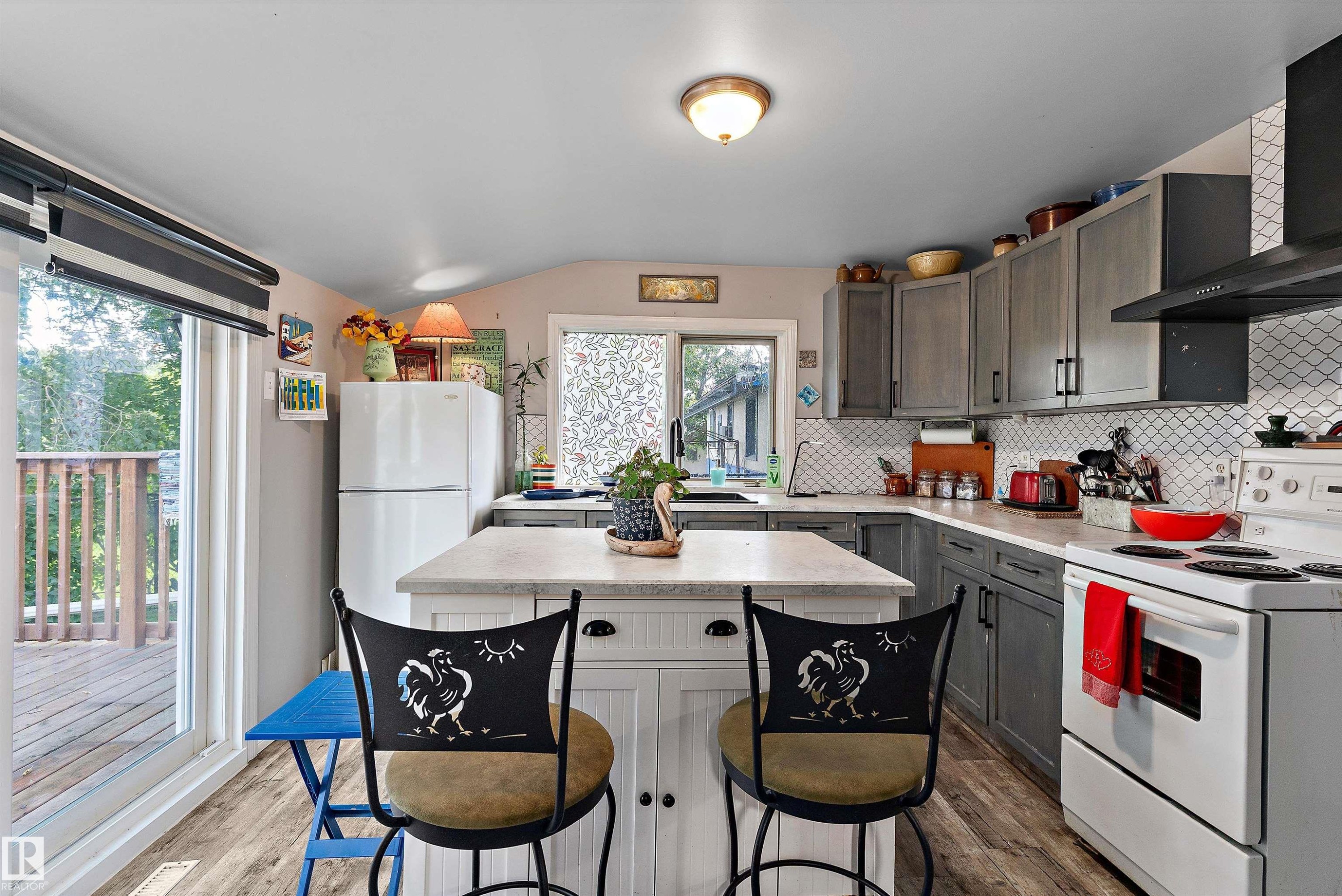 Kitchen featuring wood-finish flooring, a central island with countertop, gray cabinetry, white subway tile backsplash, and a sliding glass door to a deck - 5404 45 Avenue, Wetaskiwin, AB - Indoor Photo Showing Kitchen