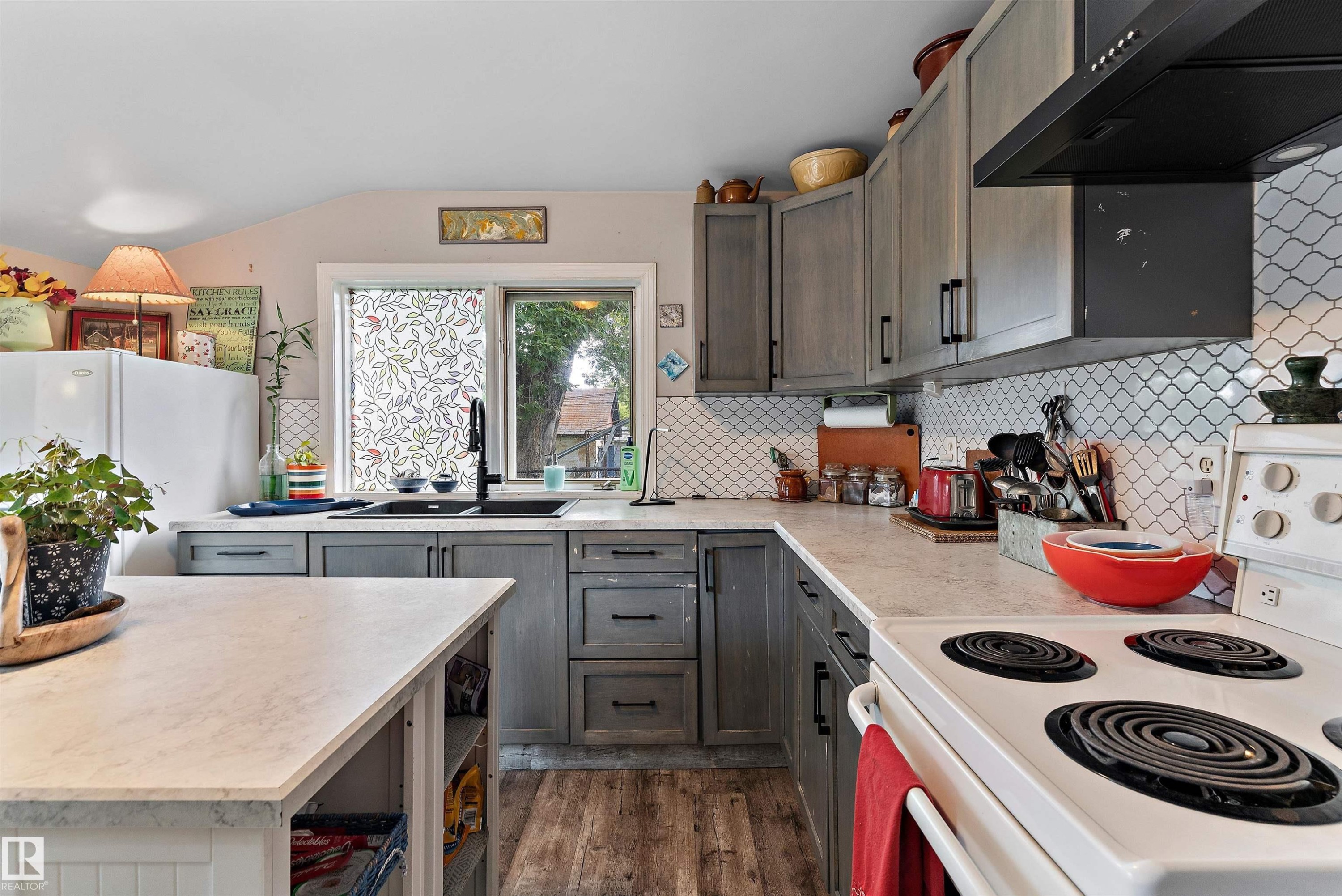 Kitchen featuring wood-finish flooring, gray cabinetry with dark hardware, a black sink, and white patterned tile backsplash - 5404 45 Avenue, Wetaskiwin, AB - Indoor Photo Showing Kitchen