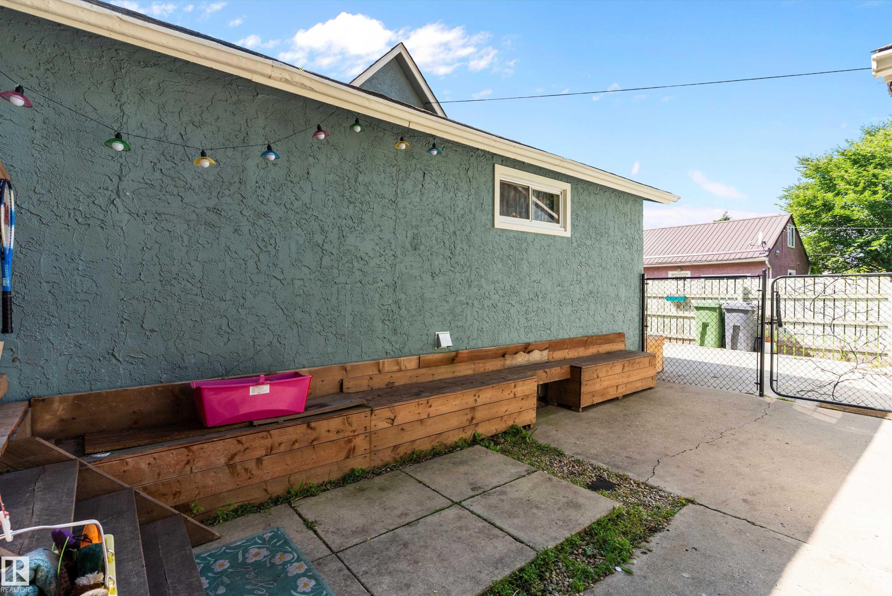 Textured exterior wall, built-in wood bench seating, concrete patio, and chain-link gate - 5404 45 Avenue, Wetaskiwin, AB - Outdoor With Deck Patio Veranda