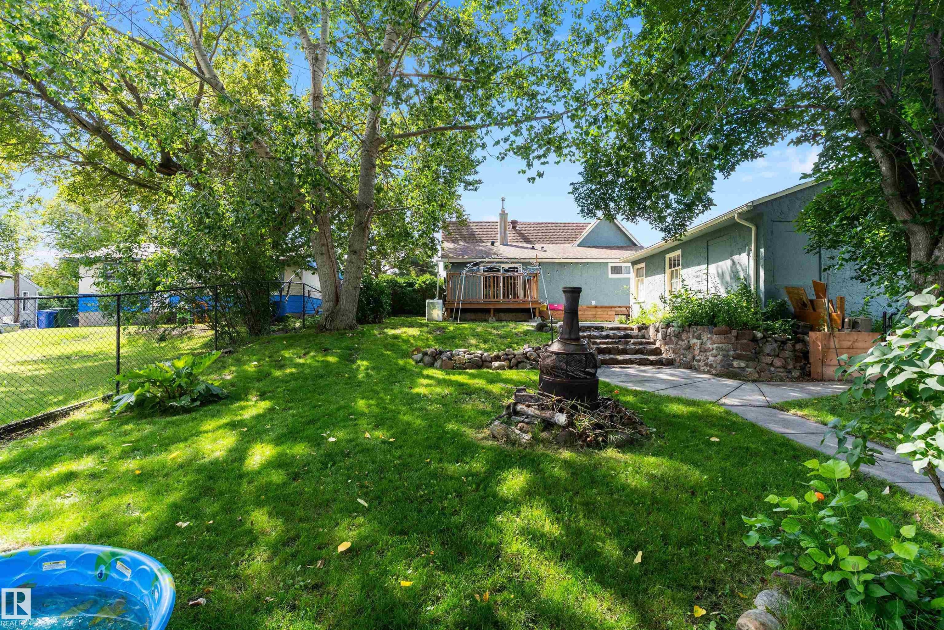 Expansive lawn area, mature trees, tiered stone steps, paved walkway, and a raised planting bed with stone retaining wall - 5404 45 Avenue, Wetaskiwin, AB - Outdoor With Deck Patio Veranda