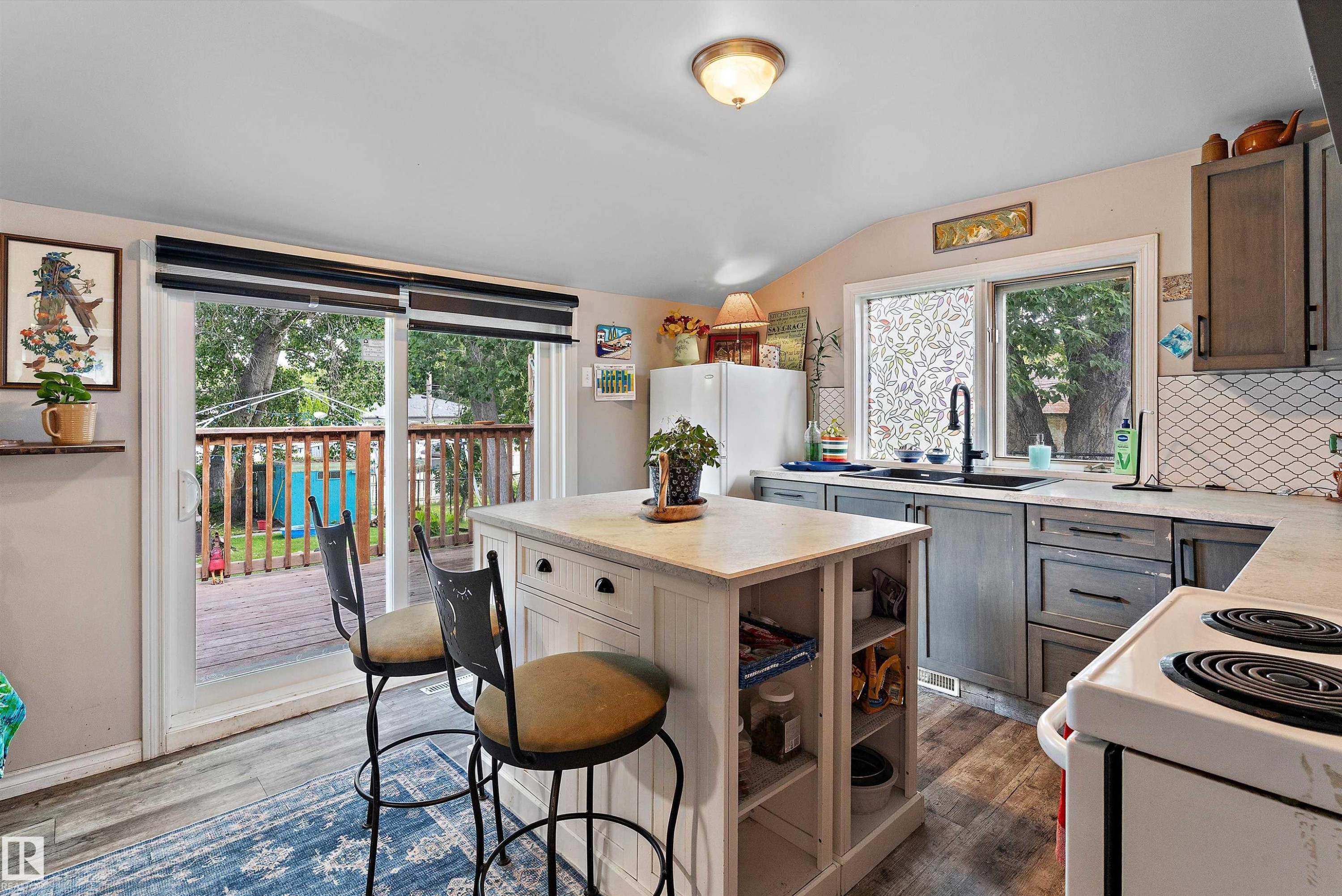 Kitchen featuring wood-finish flooring, a central island with integrated shelving, gray cabinetry, a white tile backsplash, and a sliding glass door leading to a wood deck - 5404 45 Avenue, Wetaskiwin, AB - Indoor Photo Showing Kitchen