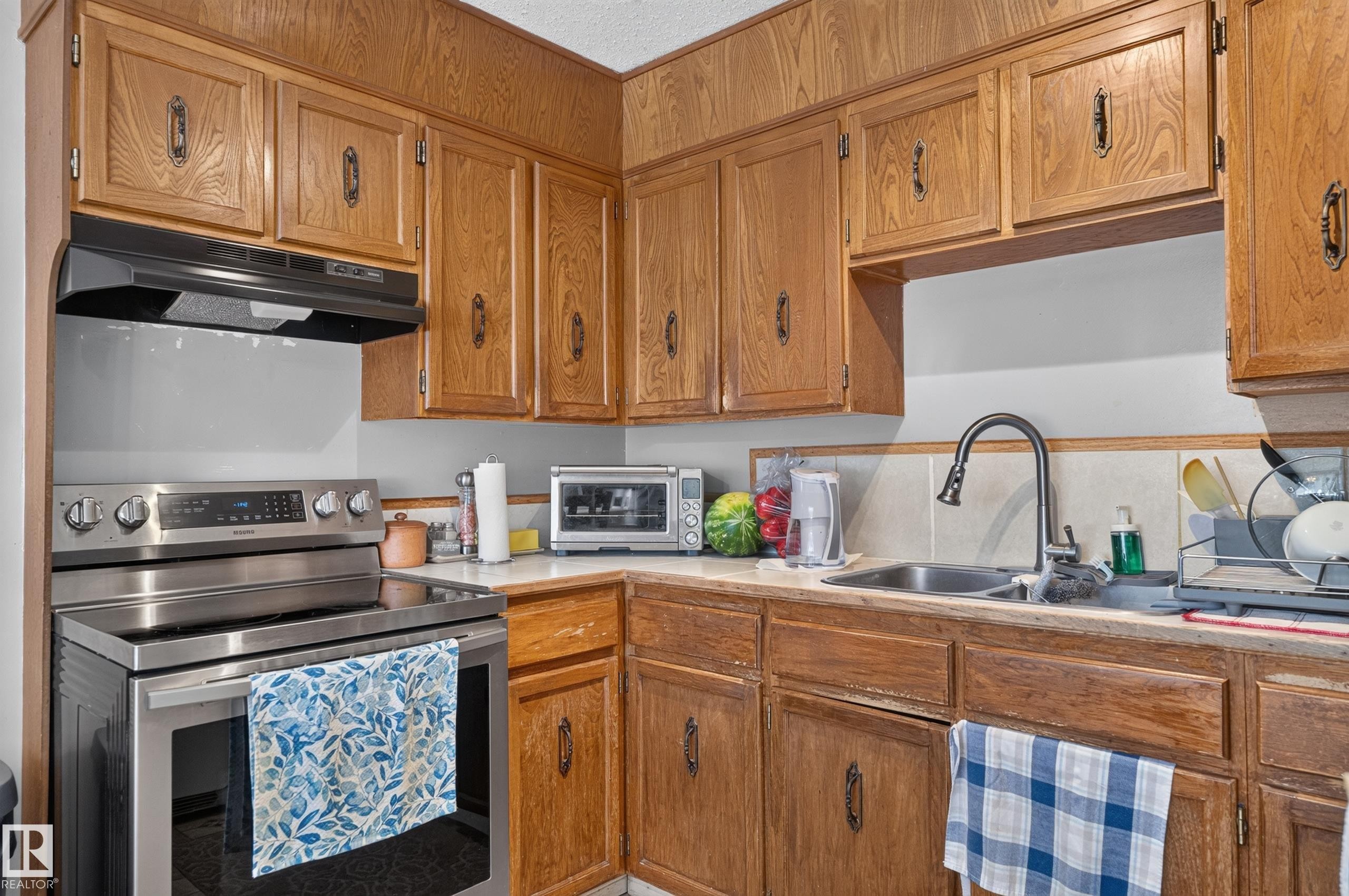 Wood-finish cabinetry with dark hardware, stainless steel range with overhead ventilation, and a stainless steel sink with a gooseneck faucet - 18247 93 Avenue Nw, Edmonton, AB - Indoor Photo Showing Kitchen With Double Sink