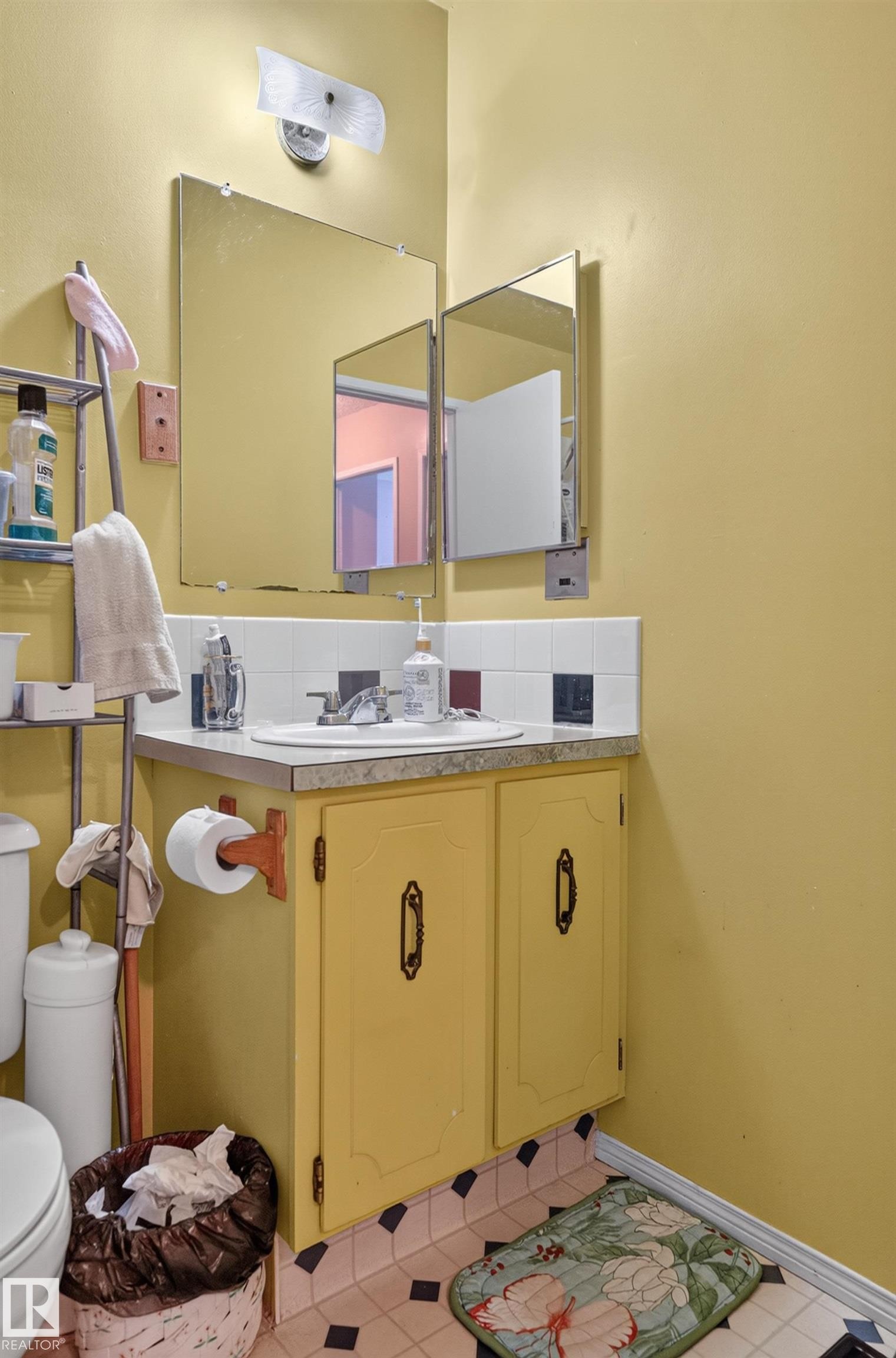 Pedestal sink with chrome faucet, a tri-fold medicine cabinet, and built-in vanity with yellow cabinetry - 18247 93 Avenue Nw, Edmonton, AB - Indoor Photo Showing Bathroom