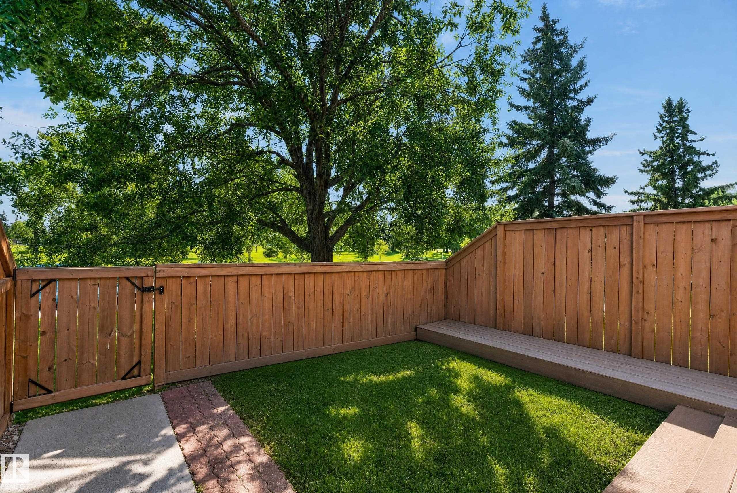 Fenced yard featuring a composite deck, mature perimeter trees, and a brick paver pathway - 18247 93 Avenue Nw, Edmonton, AB - Outdoor