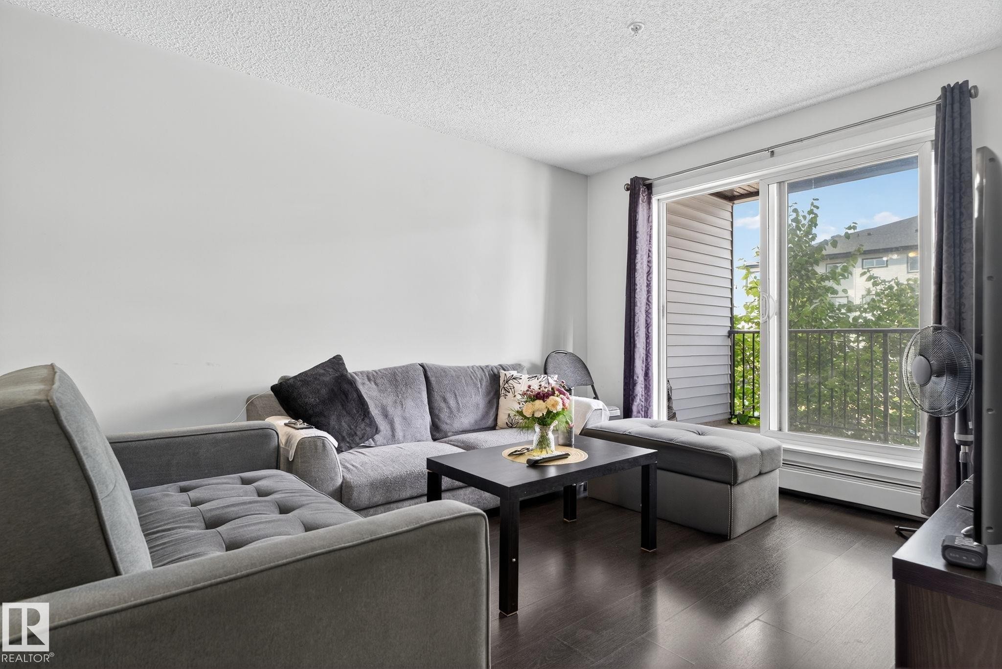 Living area featuring dark wood-finish flooring, light-colored walls, and a sliding glass door providing balcony access - 3353 16A Avenue Nw, Edmonton, AB - Indoor Photo Showing Living Room