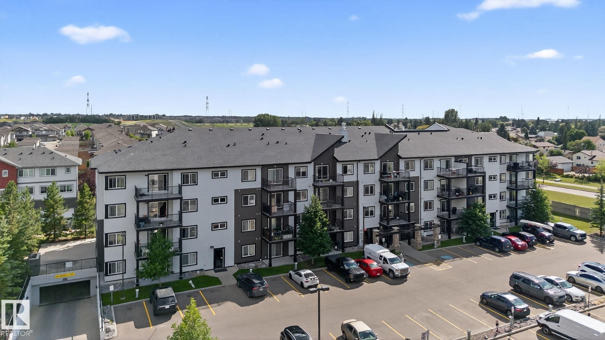 Modern multi-level building with individual private balconies, a large surface parking lot, and an integrated underground parking garage - 3353 16A Avenue Nw, Edmonton, AB - Outdoor