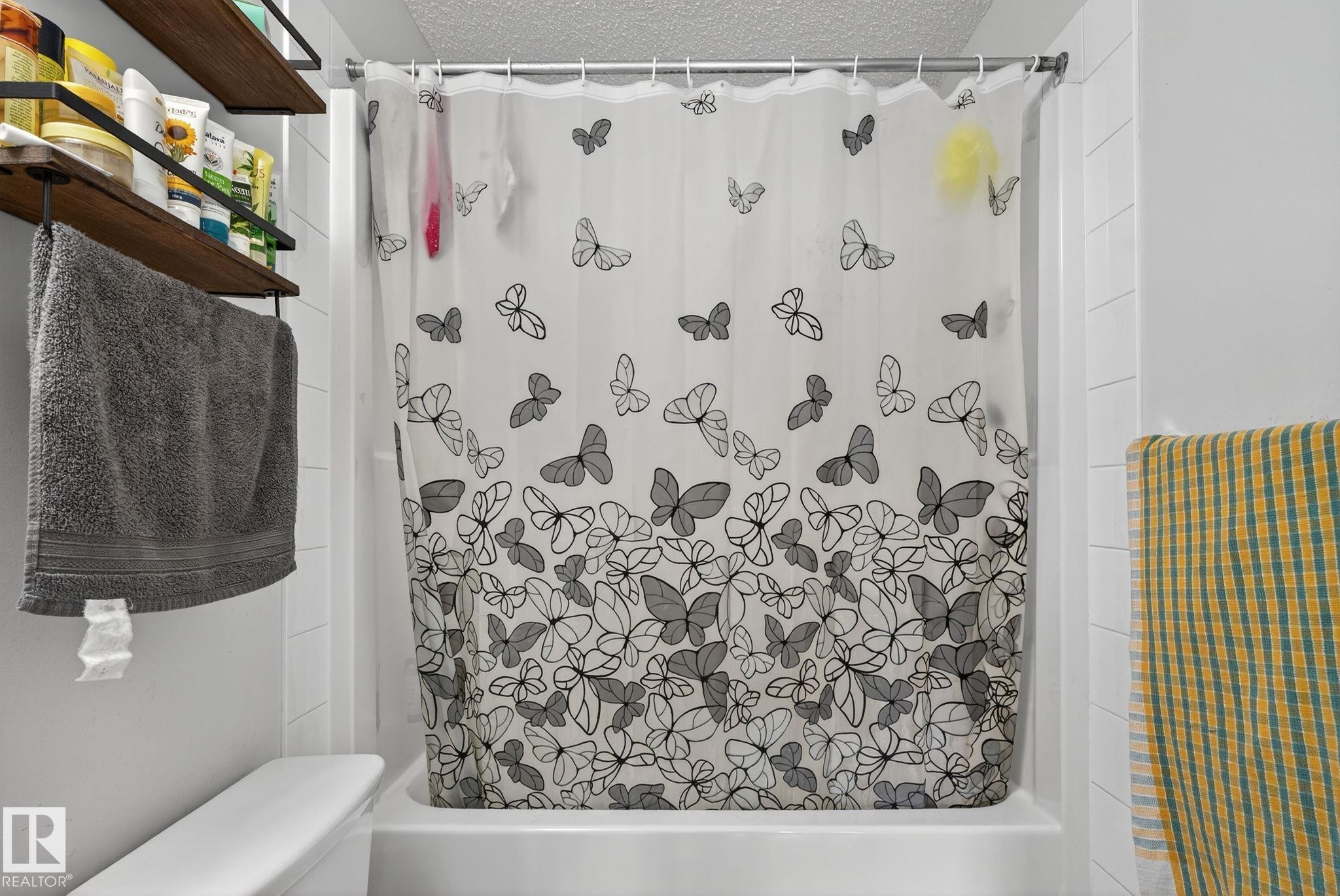 Fiberglass tub with a white shower surround, accompanied by wall-mounted shelving and a towel bar - 3353 16A Avenue Nw, Edmonton, AB - Indoor Photo Showing Bathroom