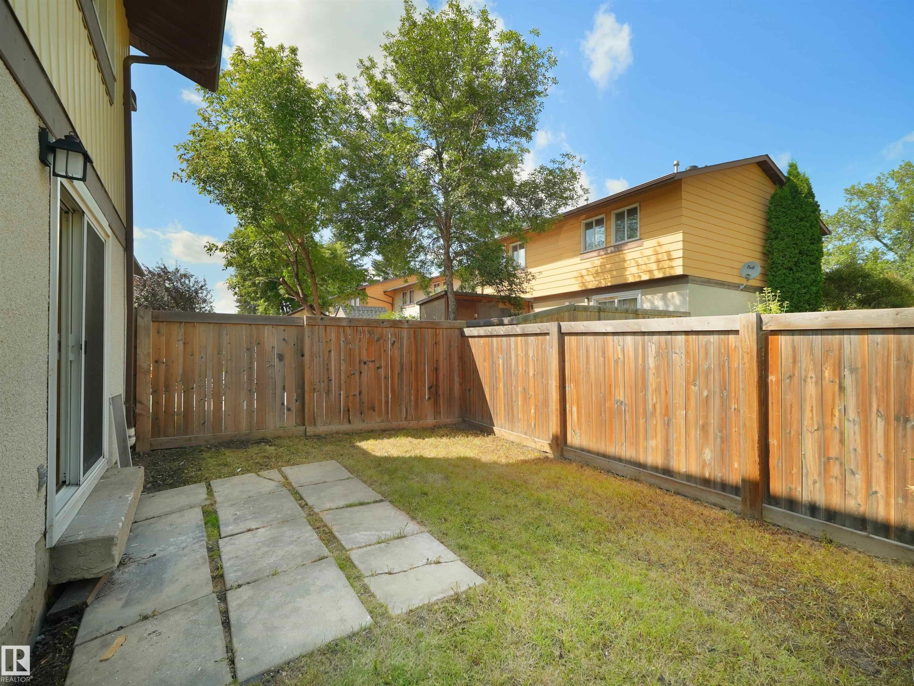 Enclosed backyard featuring a wood fence, a section of concrete pavers, and a sliding glass door - 126 Woodstock Nw, Edmonton, AB - Outdoor