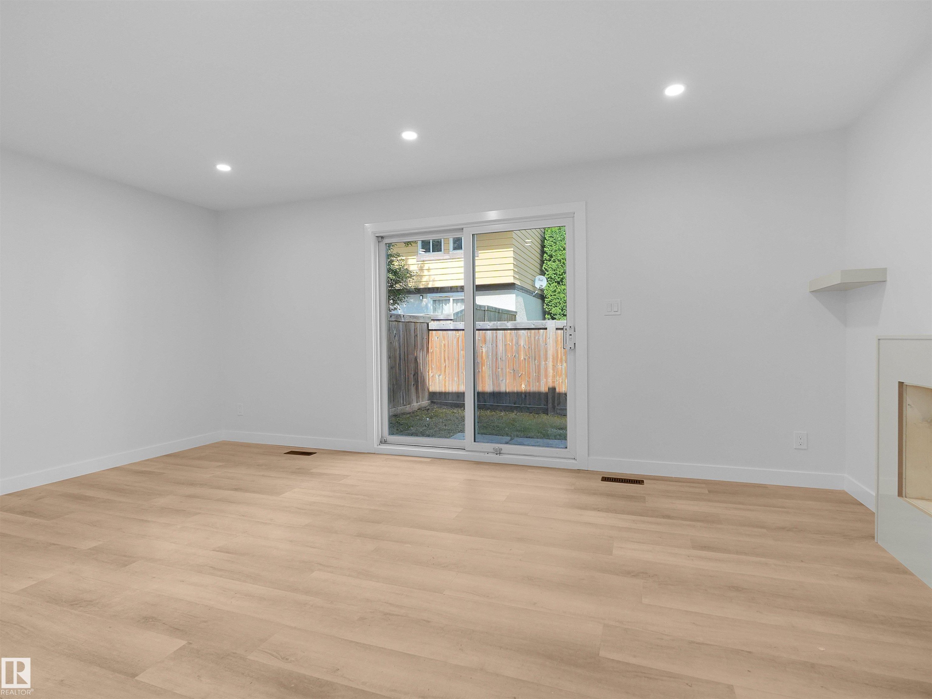 Light wood-finish flooring, recessed ceiling lighting, sliding glass door, and a built-in fireplace feature with a mantel - 126 Woodstock Nw, Edmonton, AB - Indoor Photo Showing Other Room With Fireplace