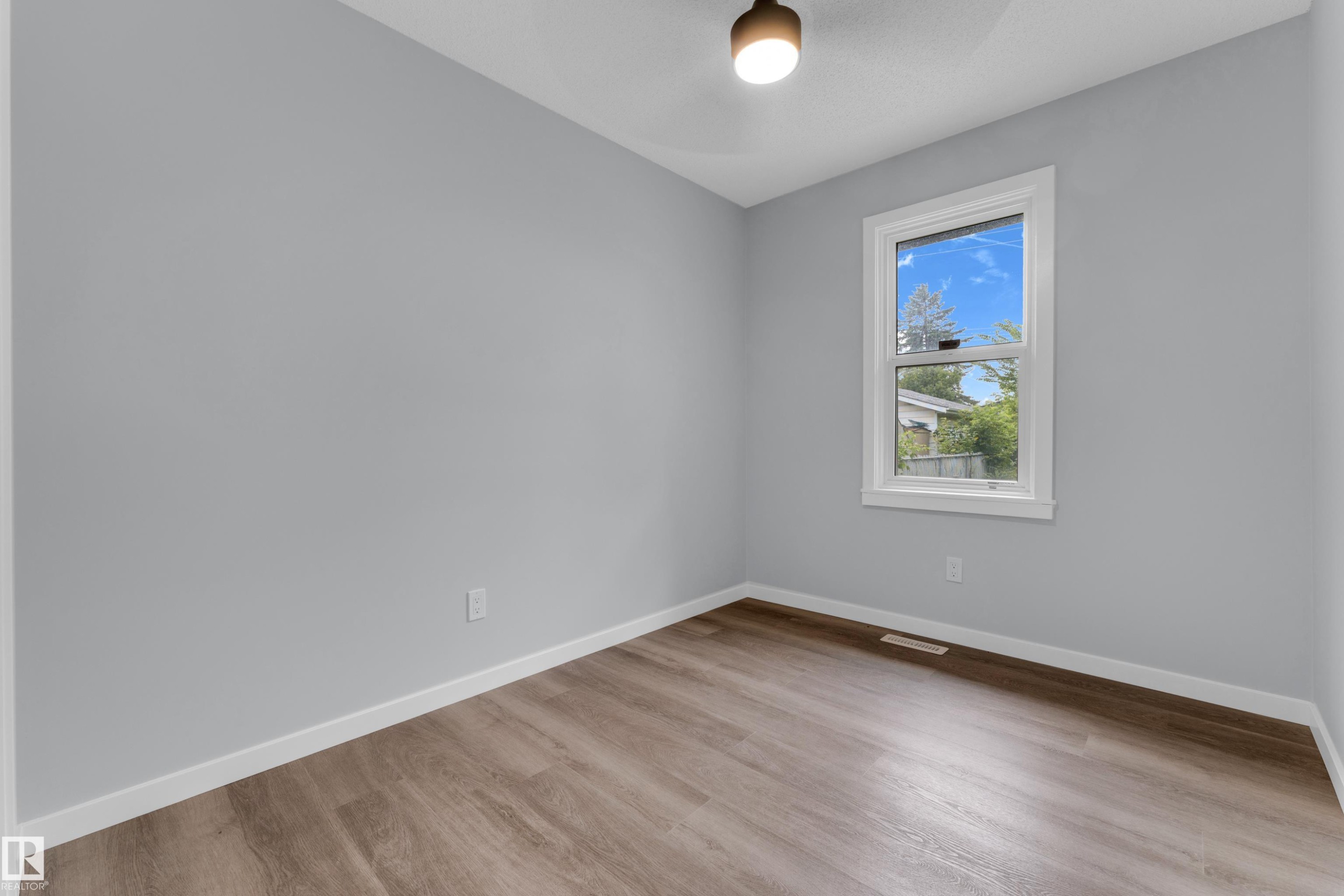 Room with light gray walls, wood-finish flooring, a single window with white trim, and a contemporary ceiling light fixture - 9416 153 Street Nw, Edmonton, AB - Indoor Photo Showing Other Room