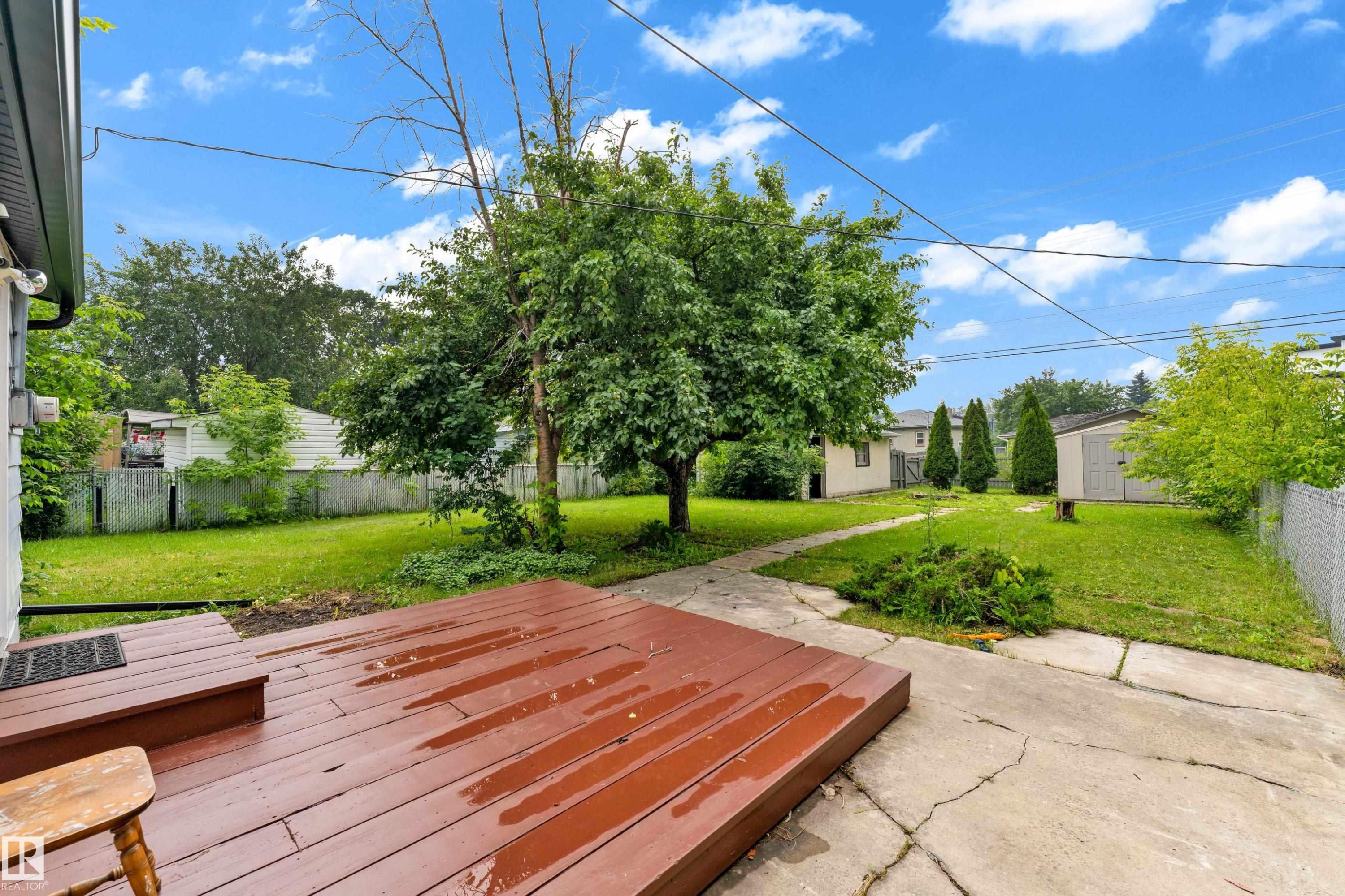 Expansive backyard featuring a red-stained wooden deck, concrete patio, and a chain-link fence - 9416 153 Street Nw, Edmonton, AB - Outdoor