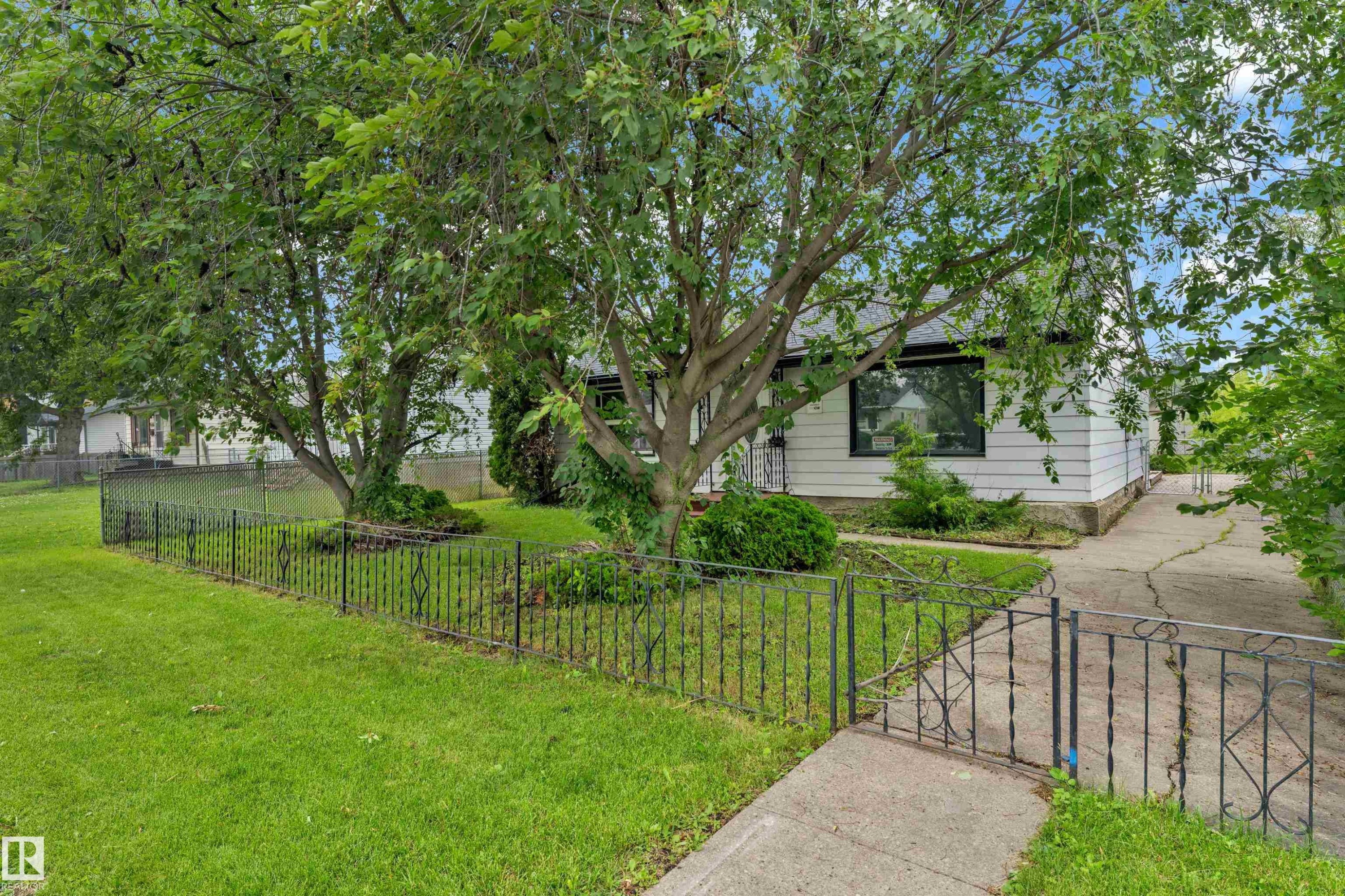 White-sided residence featuring a dark-framed window, mature trees, and a decorative wrought iron fence - 9416 153 Street Nw, Edmonton, AB - Outdoor