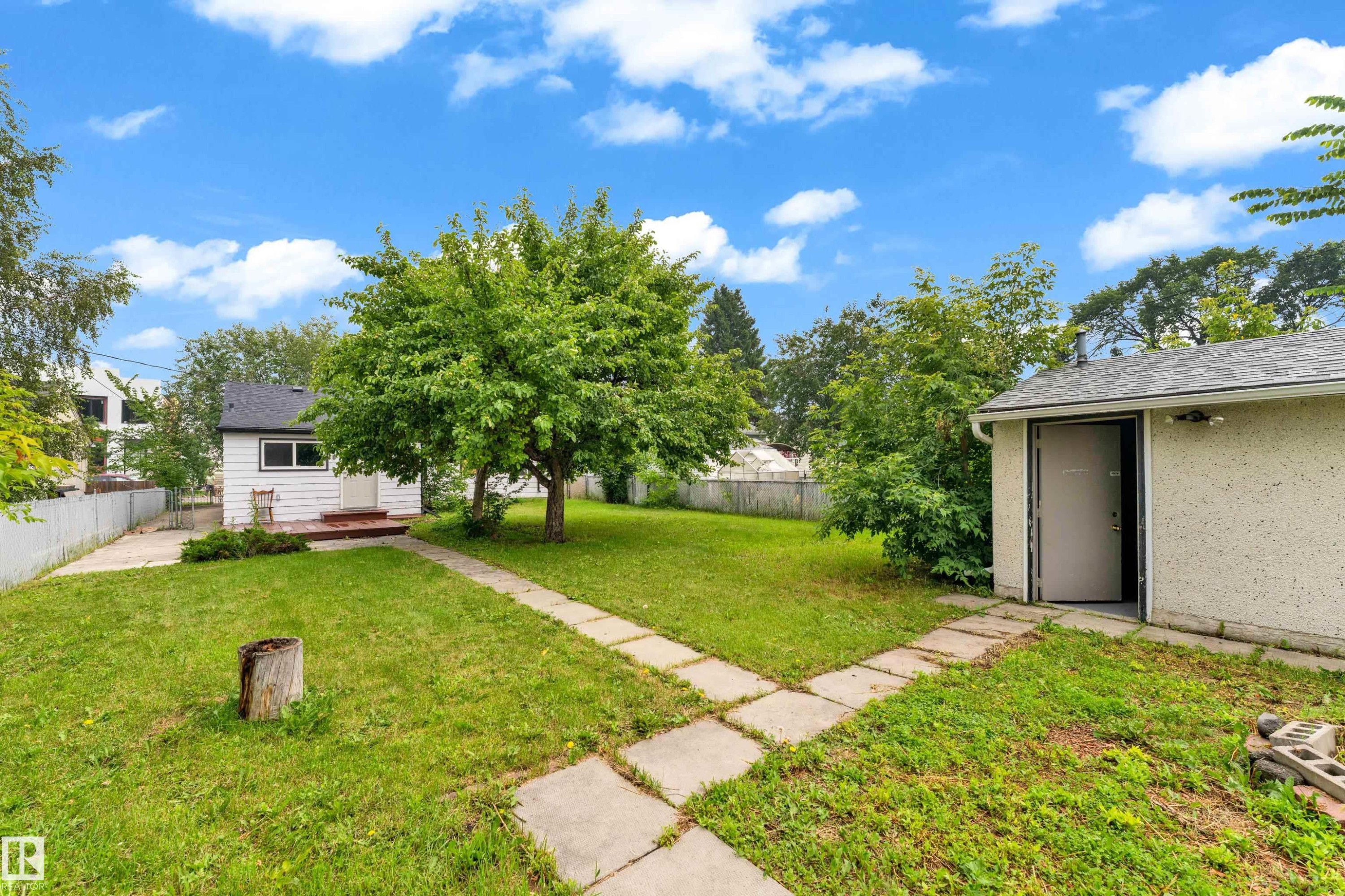 Expansive backyard featuring a central mature tree, a concrete paver pathway, and a detached outbuilding with a single entrance - 9416 153 Street Nw, Edmonton, AB - Outdoor