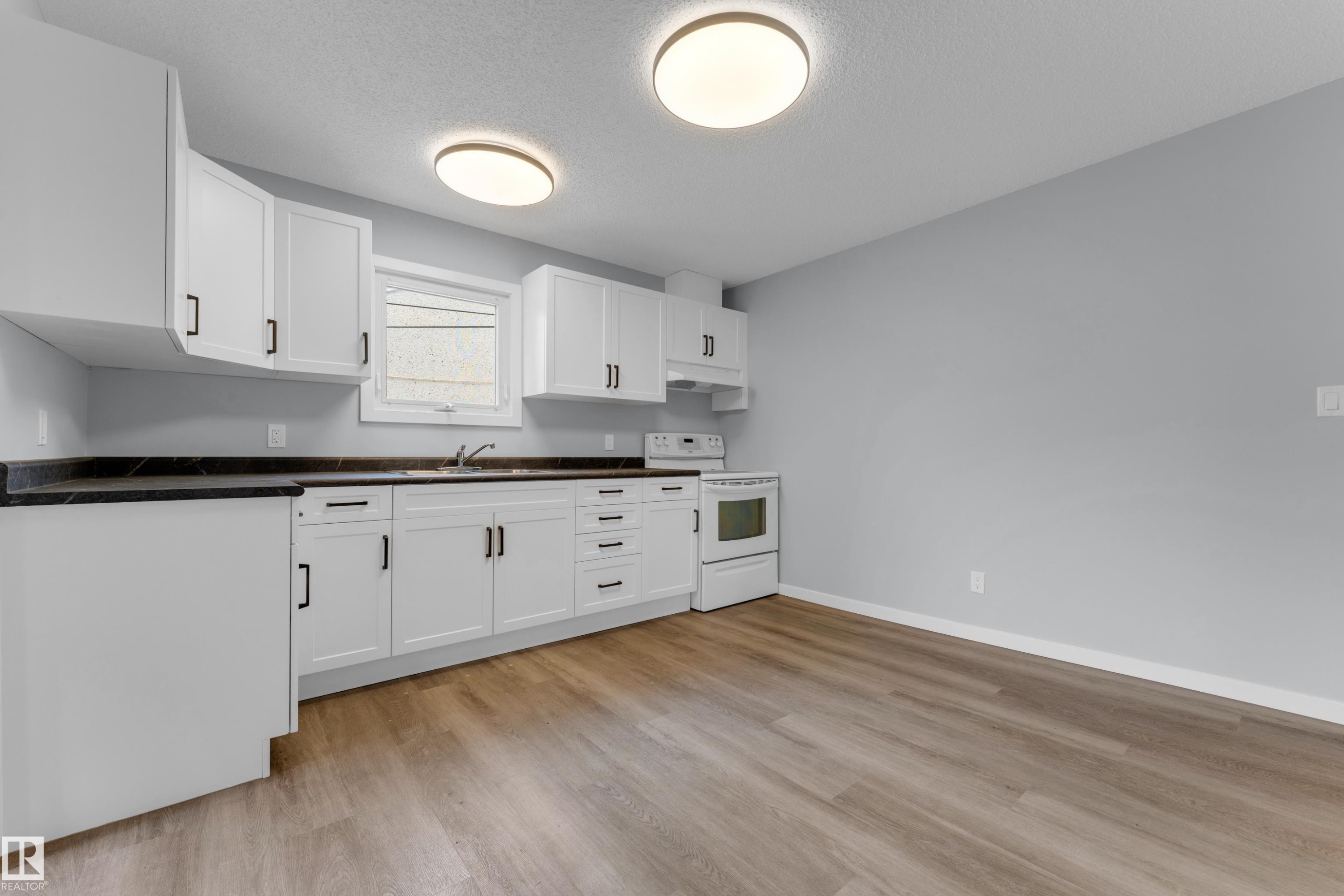 Kitchen featuring white shaker-style cabinetry, dark countertops, a white range, wood-finish flooring, and two flush-mount ceiling lights - 9416 153 Street Nw, Edmonton, AB - Indoor Photo Showing Kitchen