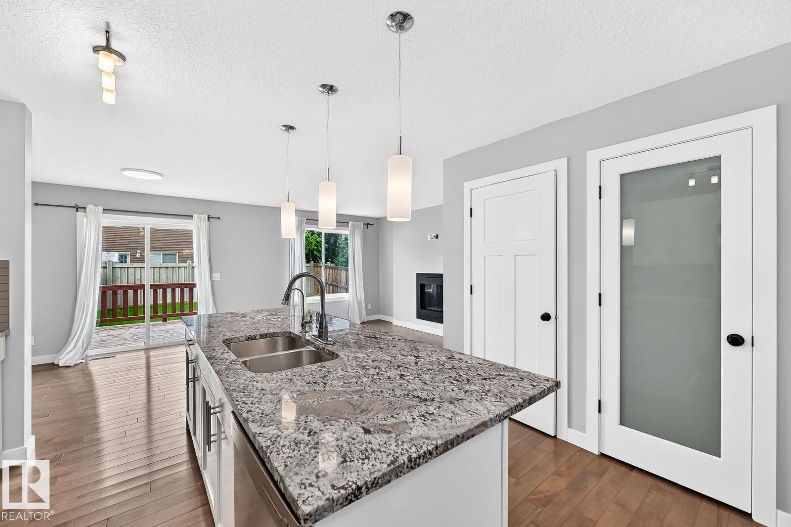 Kitchen island with dual stainless steel sink and stone countertop, wood-finish flooring, and white paneled doors - 1112 176 Street Sw, Edmonton, AB - Indoor Photo Showing Kitchen With Double Sink With Upgraded Kitchen