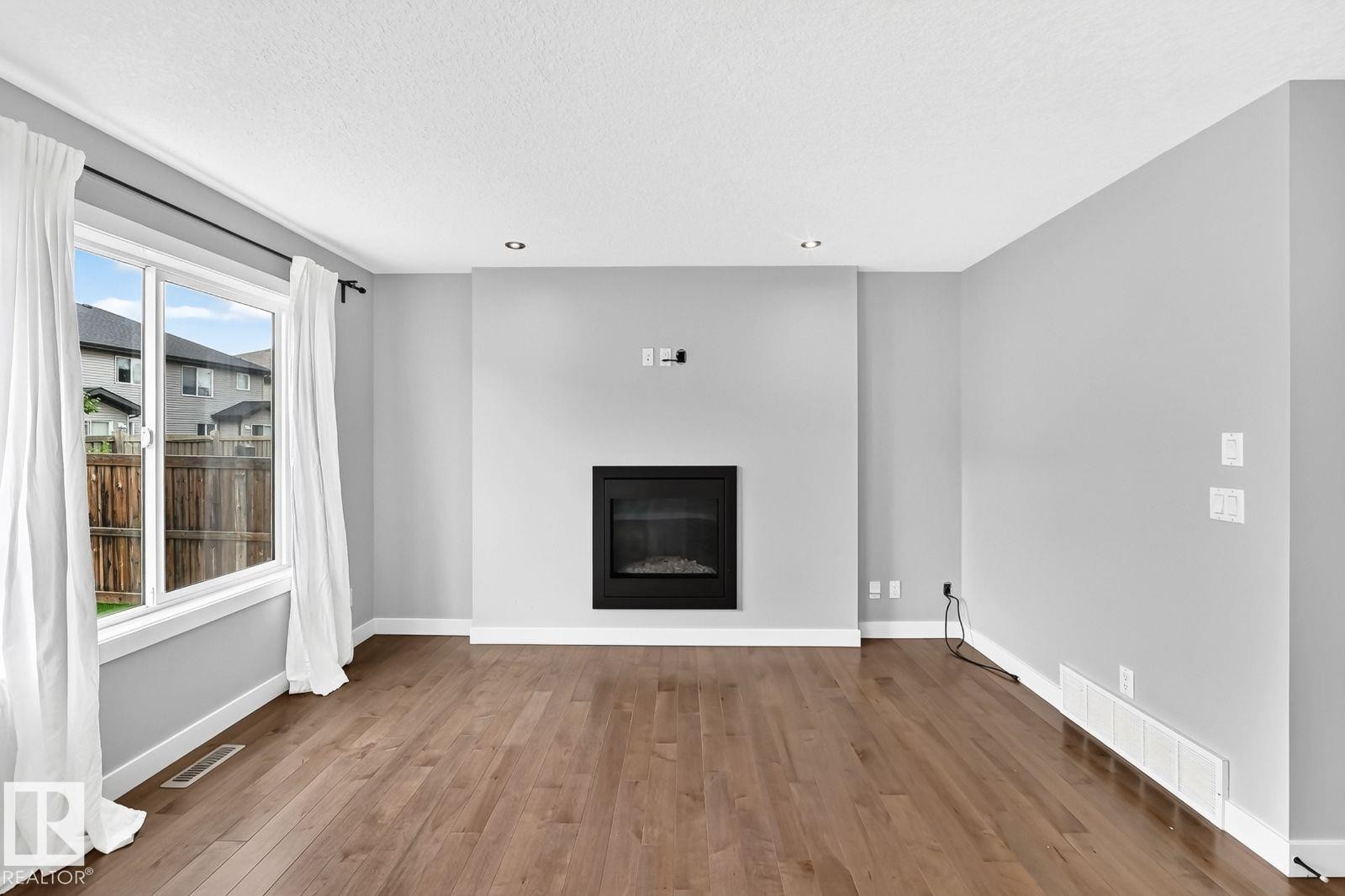 Wood-finish flooring throughout, recessed ceiling lighting, an integrated electric fireplace, and a large window - 1112 176 Street Sw, Edmonton, AB - Indoor Photo Showing Living Room