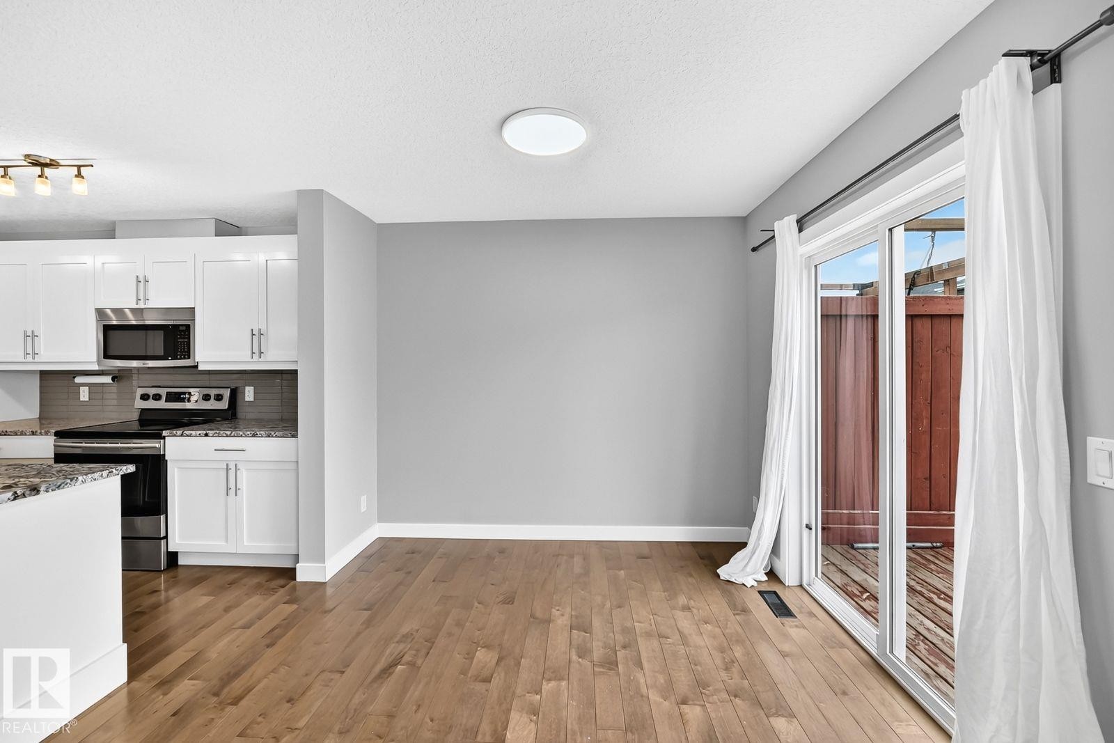 Kitchen featuring white cabinetry, stainless steel microwave, black range, granite countertops, and tile backsplash - 1112 176 Street Sw, Edmonton, AB - Indoor Photo Showing Kitchen