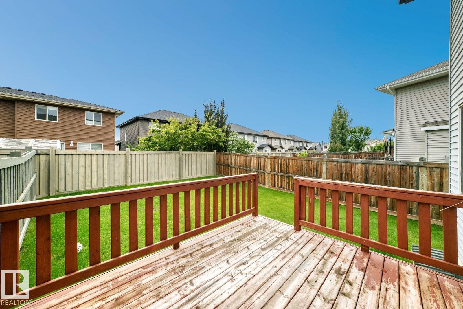Expansive wood deck with a red-stained railing, opening to a grass yard, enclosed by wood fencing - 1112 176 Street Sw, Edmonton, AB - Outdoor With Deck Patio Veranda With Exterior