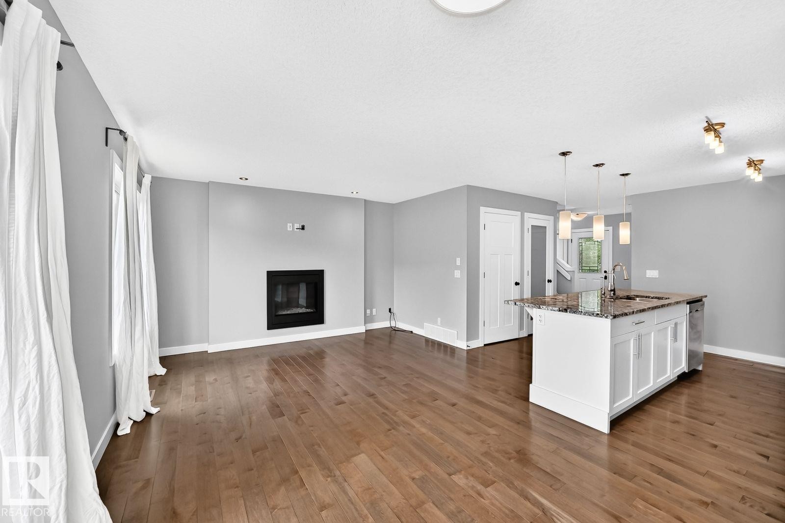Hardwood flooring, fireplace, kitchen island with pendant lighting, white cabinetry, and stainless steel dishwasher - 1112 176 Street Sw, Edmonton, AB - Indoor With Fireplace