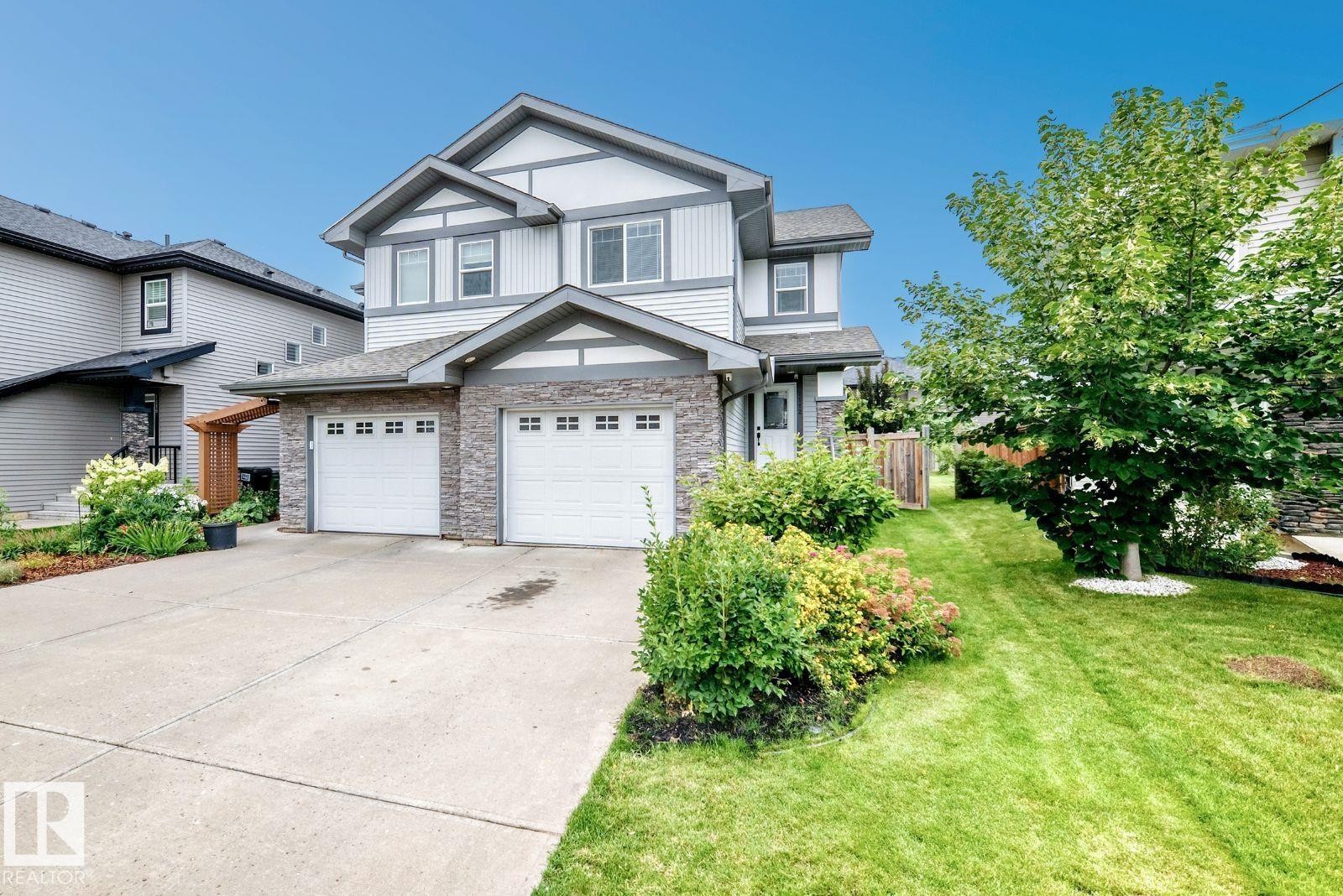 Multi-level facade with siding and stone accents, dual garage doors, concrete driveway, and established landscaping - 1112 176 Street Sw, Edmonton, AB - Outdoor With Facade