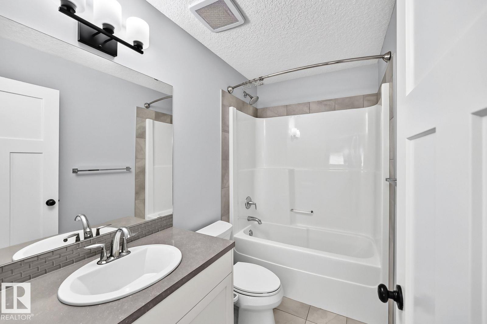 Bathroom featuring a vanity with an oval basin, a rectangular mirror, and a three-light fixture - 1112 176 Street Sw, Edmonton, AB - Indoor Photo Showing Bathroom