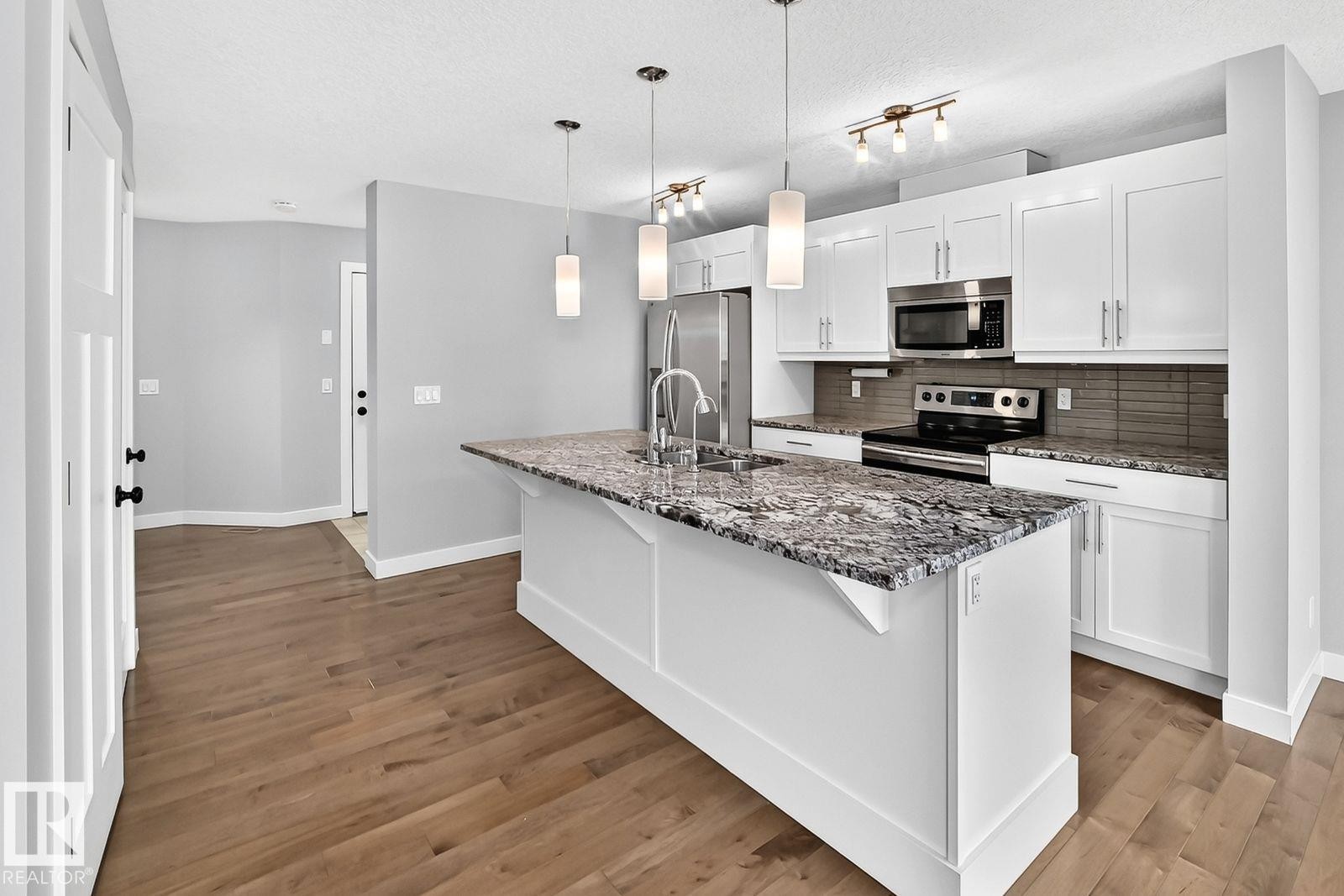 Kitchen featuring a central island with a stone countertop, stainless steel appliances, and white cabinetry - 1112 176 Street Sw, Edmonton, AB - Indoor Photo Showing Kitchen With Upgraded Kitchen