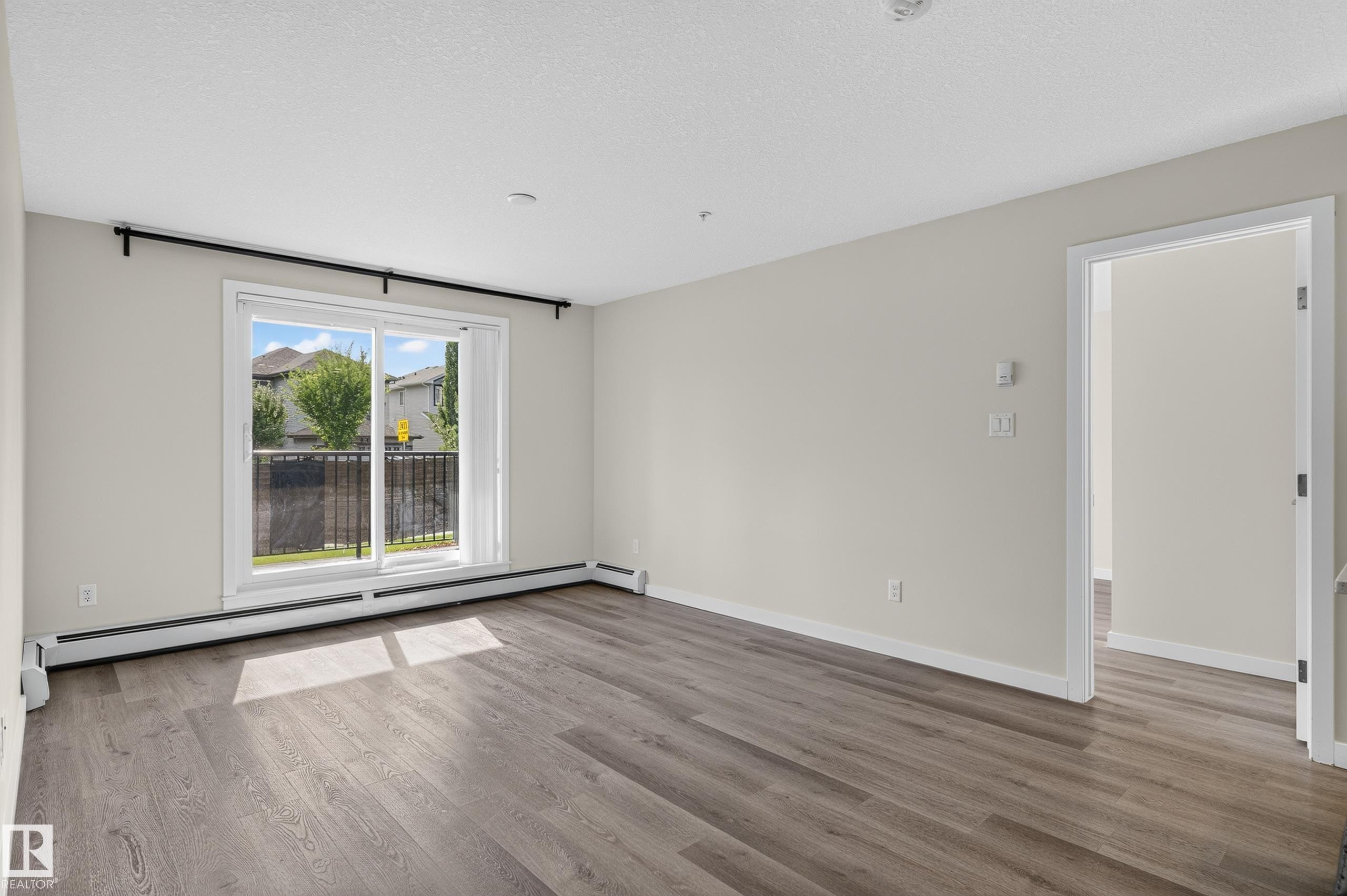 Wood-finish flooring throughout, light neutral wall paint, and a sliding glass door providing natural illumination - #131 5504 Schonsee Dr Nw, Edmonton, AB - Indoor Photo Showing Other Room