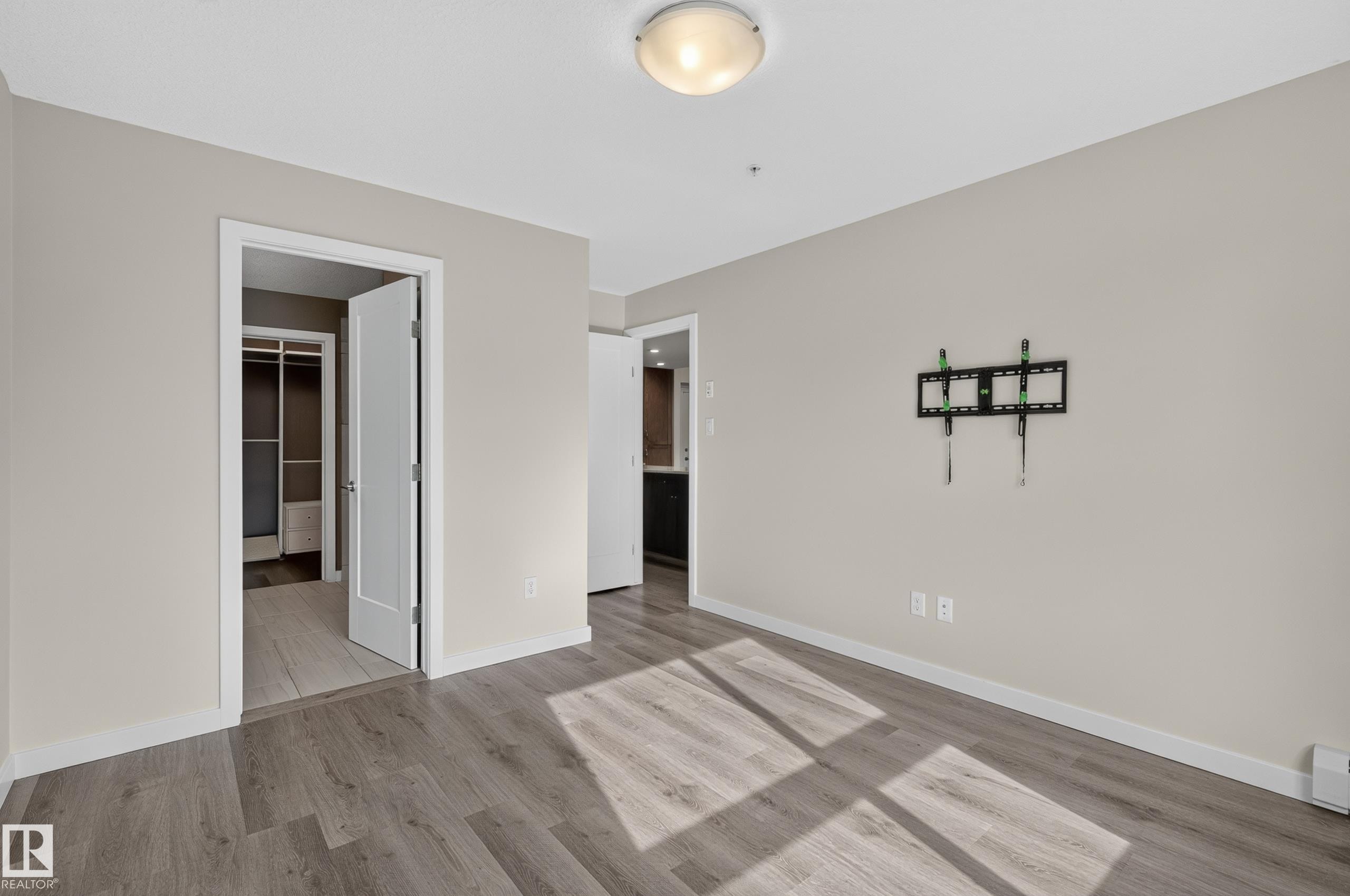 Wood-finish flooring throughout, neutral painted walls, and white trim - #131 5504 Schonsee Dr Nw, Edmonton, AB - Indoor Photo Showing Other Room