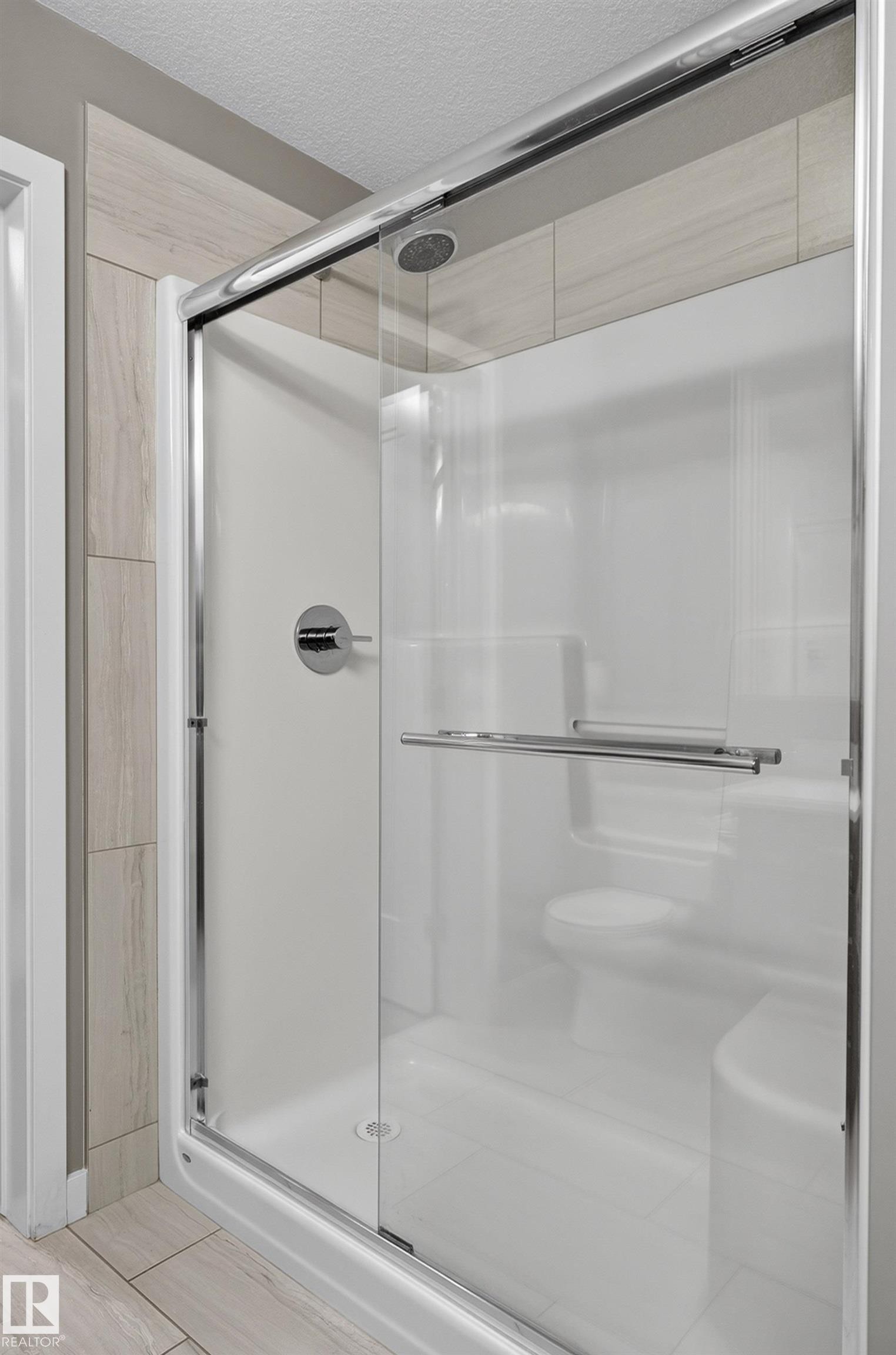 Enclosed shower with sliding glass doors, built-in seating, chrome fixtures, and tiled surround - #131 5504 Schonsee Dr Nw, Edmonton, AB - Indoor Photo Showing Bathroom