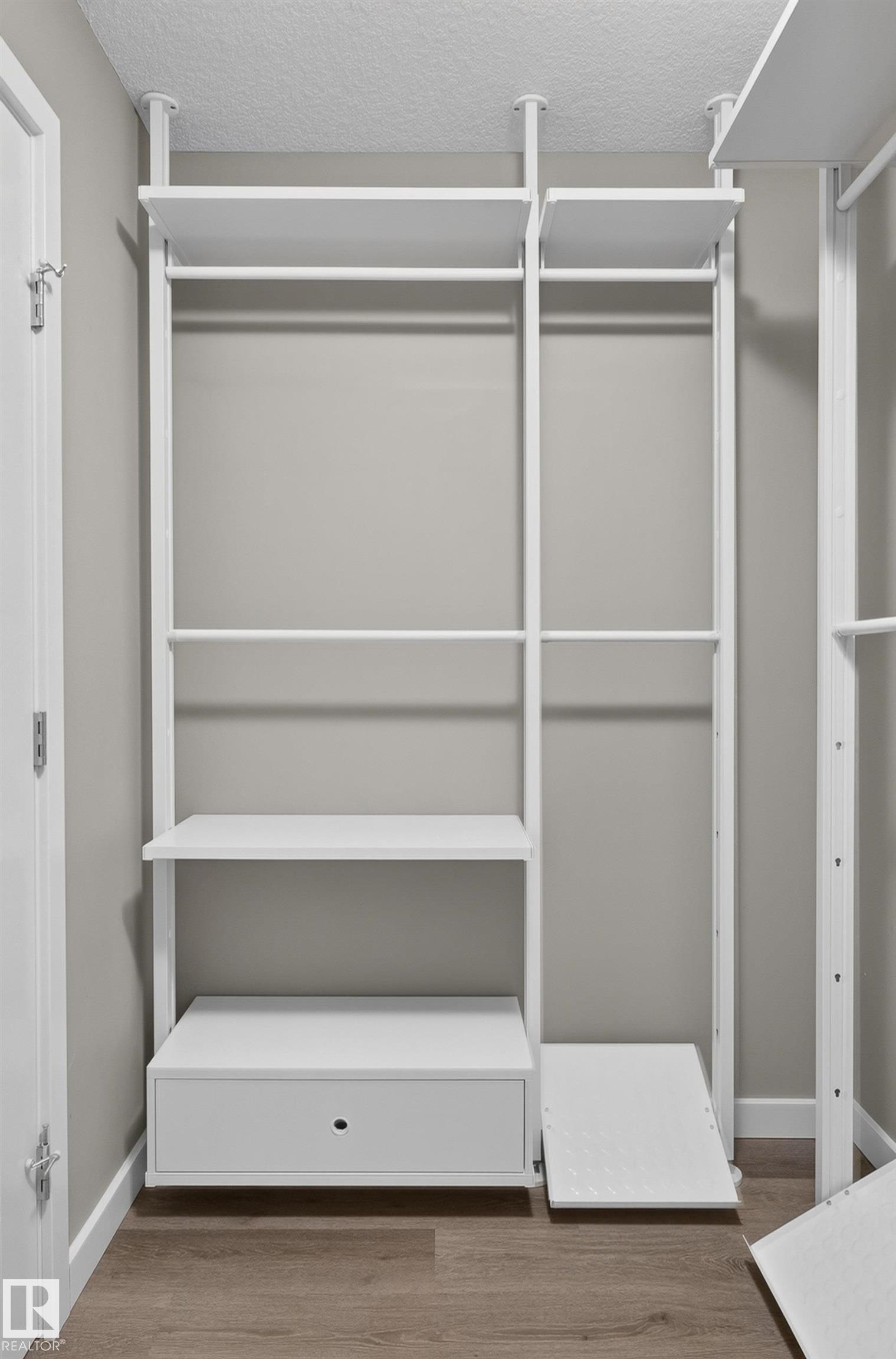 Integrated white closet system featuring multiple shelves, hanging rods, and a drawer - #131 5504 Schonsee Dr Nw, Edmonton, AB - Indoor With Storage
