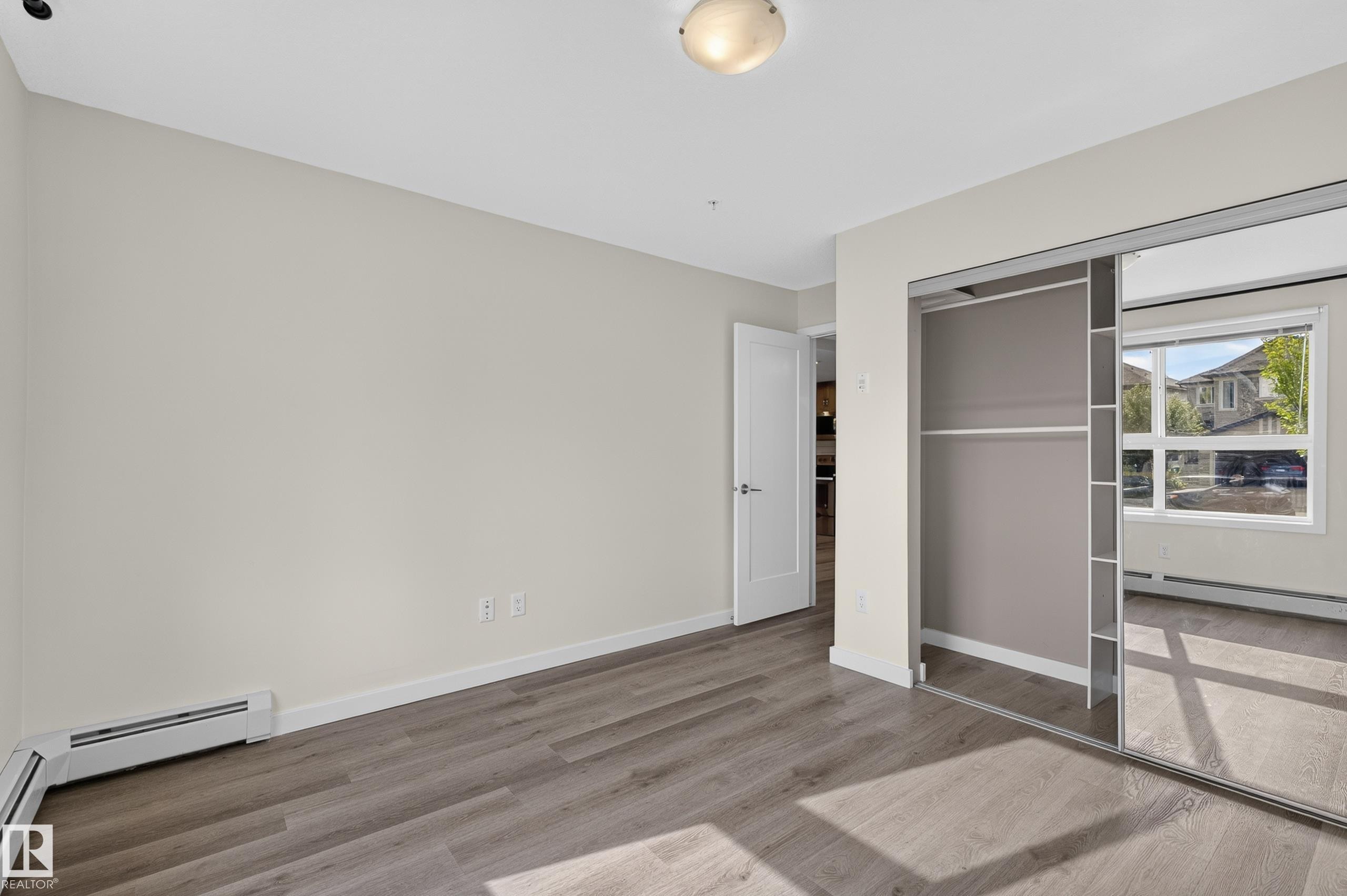 Wood-finish flooring, mirrored closet doors, and light-toned walls - #131 5504 Schonsee Dr Nw, Edmonton, AB - Indoor Photo Showing Other Room