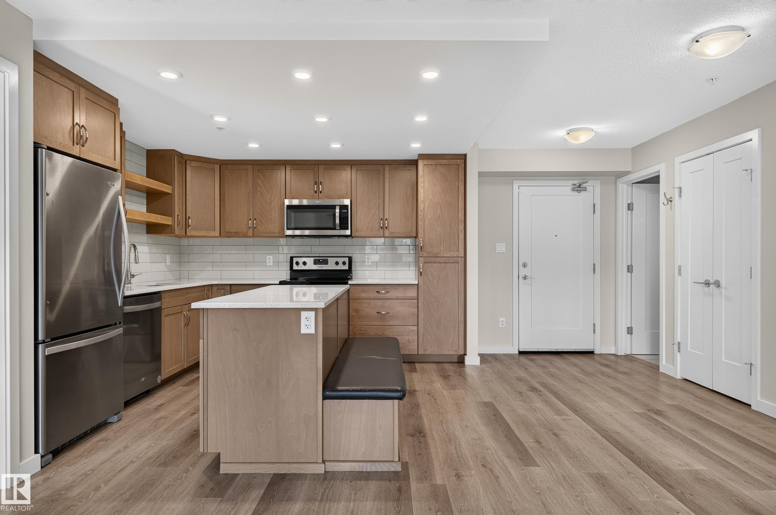 Modern kitchen featuring wood-finish cabinetry, stainless steel appliances, white subway tile backsplash, and light-colored countertops - #131 5504 Schonsee Dr Nw, Edmonton, AB - Indoor Photo Showing Kitchen With Stainless Steel Kitchen