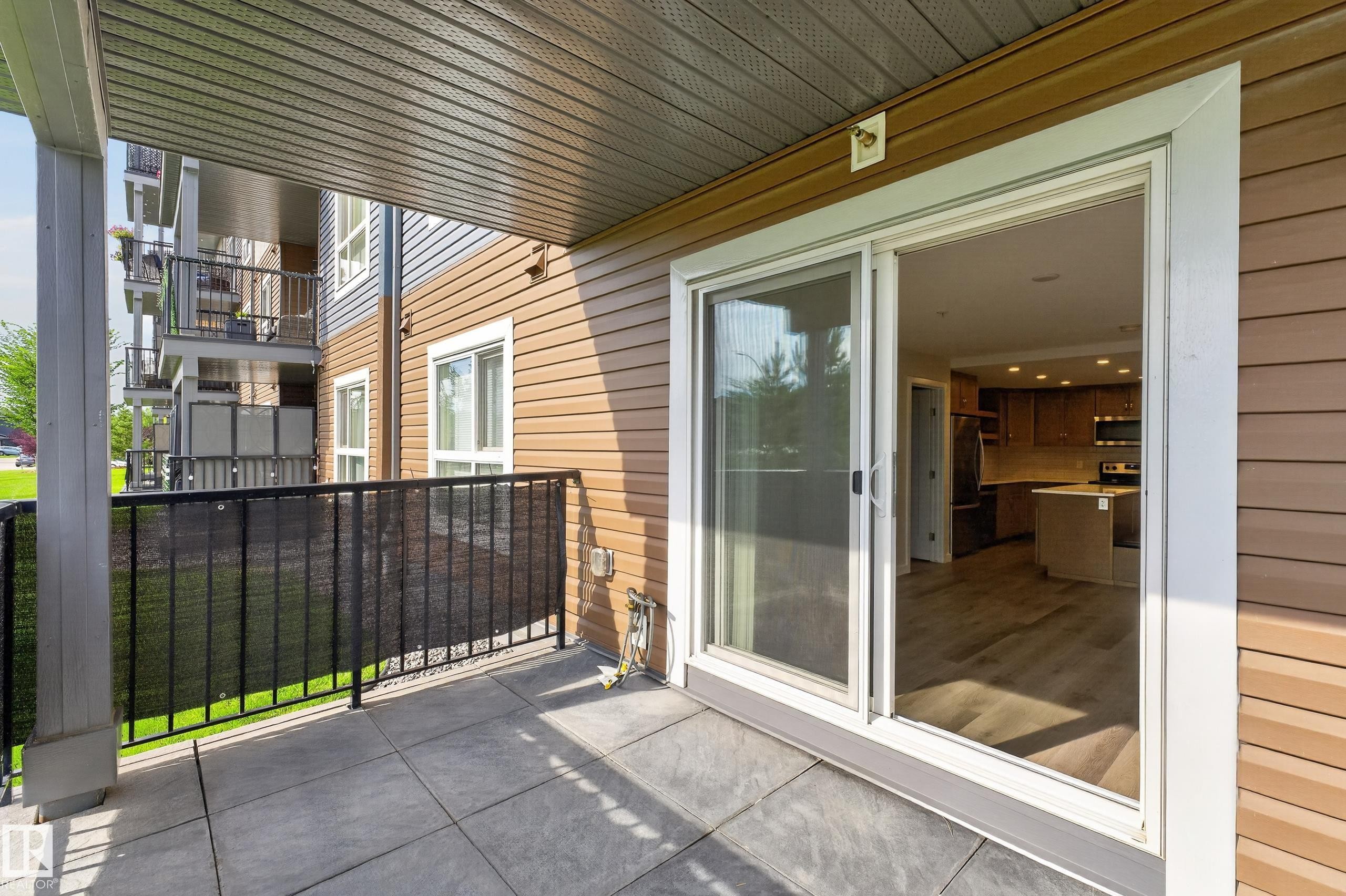 Ground-level patio with square paver flooring and black metal railing - #131 5504 Schonsee Dr Nw, Edmonton, AB - Outdoor With Balcony With Exterior